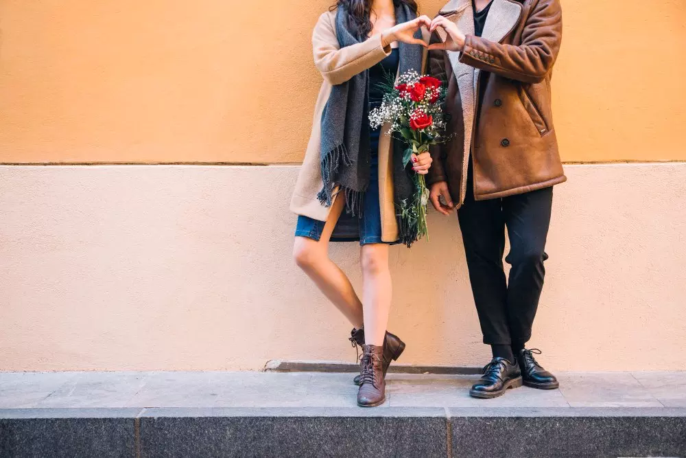 Coppia che forma un cuore con le mani mentre tiene un bouquet di rose rosse.