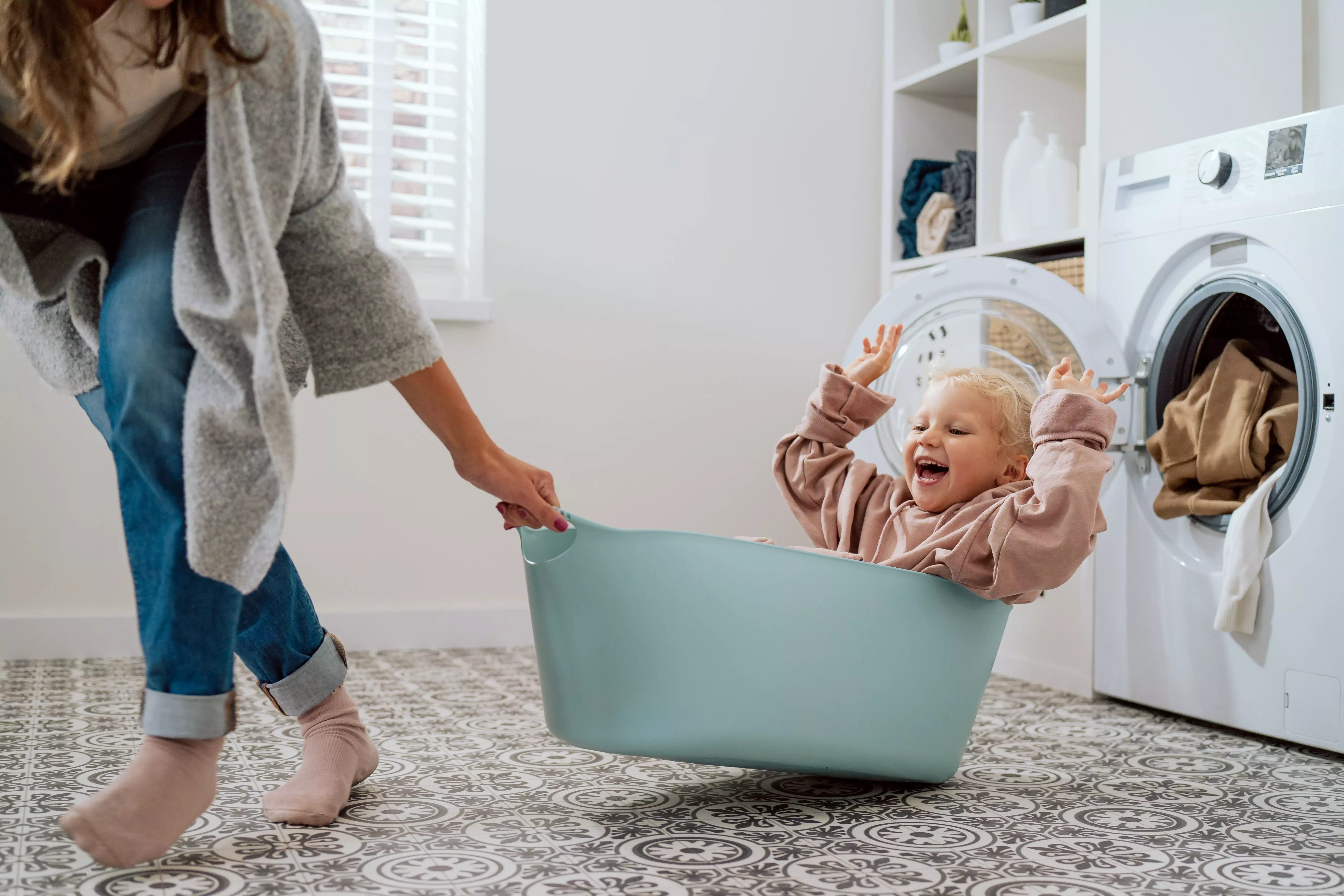 Pepco child sitting in a laundry basket being pulled across a utility room floor during playtime.