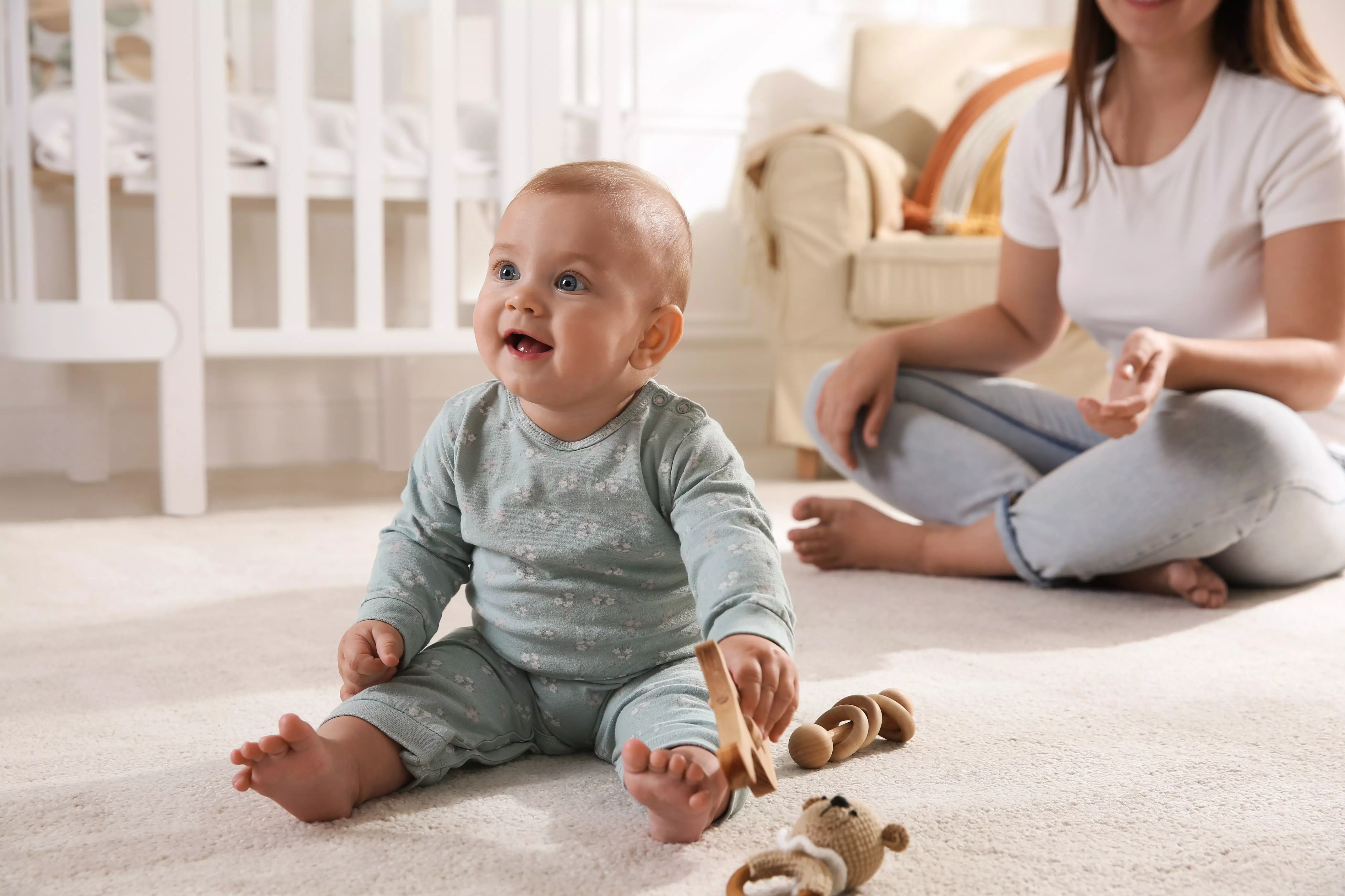 Pepco baby wearing sage green printed pyjamas sitting on floor playing with wooden toys near parent.