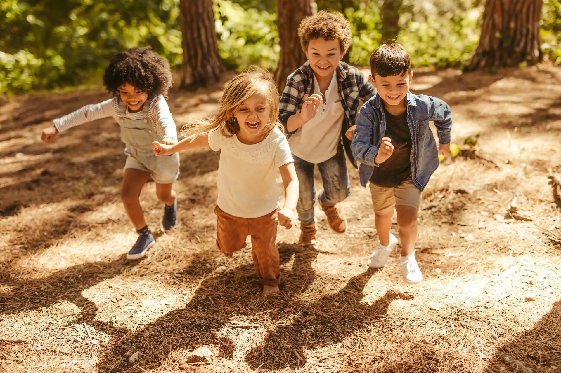 Children running joyfully through a forest wearing Pepco casual clothing including shirts, shorts and denim items.