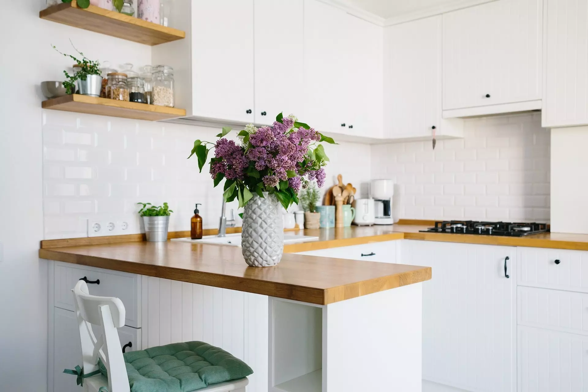 Pepco home kitchen design with white cabinets, wooden countertops and purple lilac flowers in a textured vase.