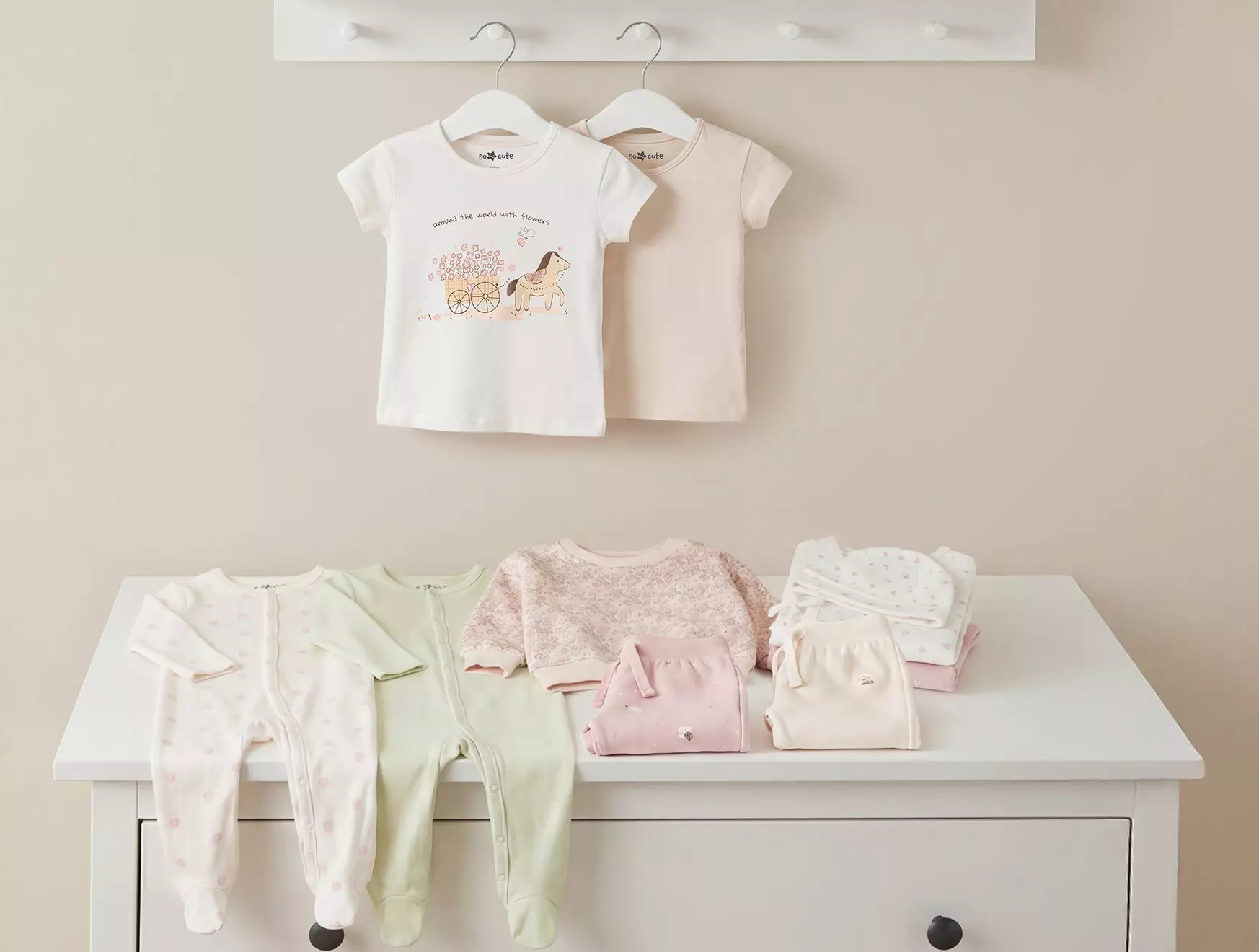Kolekcja dziecięcej odzieży Pepco w pastelowych kolorach, z koszulkami, śpioszkami i akcesoriami dla niemowląt.