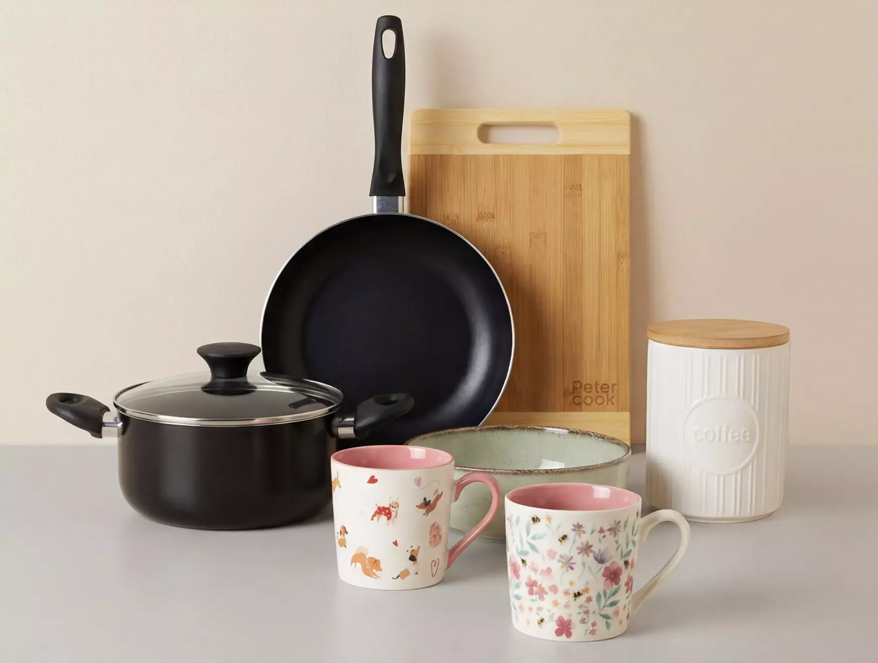 Kolekcja akcesoriów kuchennych Pepco: patelnia, garnek, deska do krojenia, pojemnik na kawę i dwa ozdobne kubki z różowymi motywami.