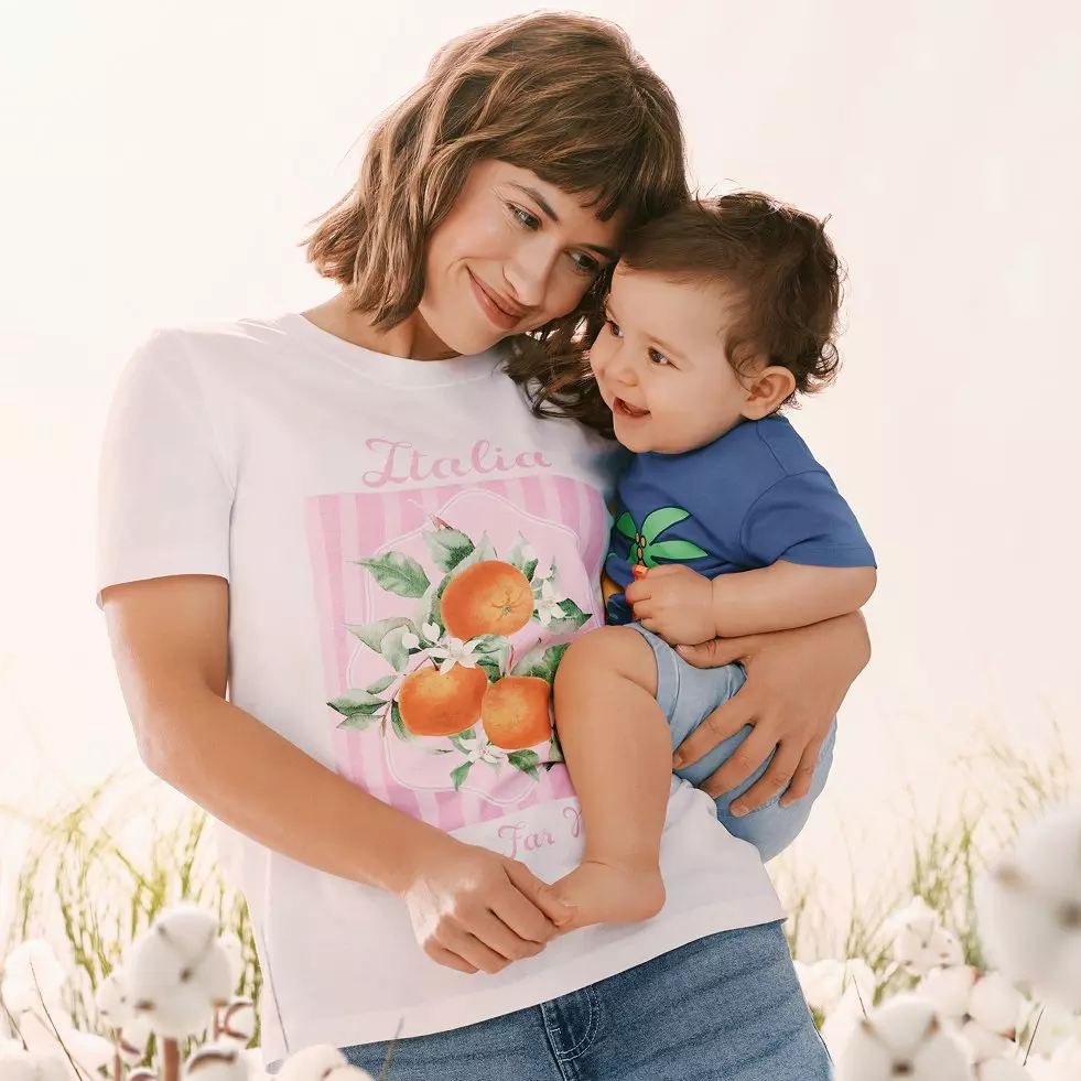 Woman holding toddler, wearing white t-shirt with Italia orange print, child in blue top.