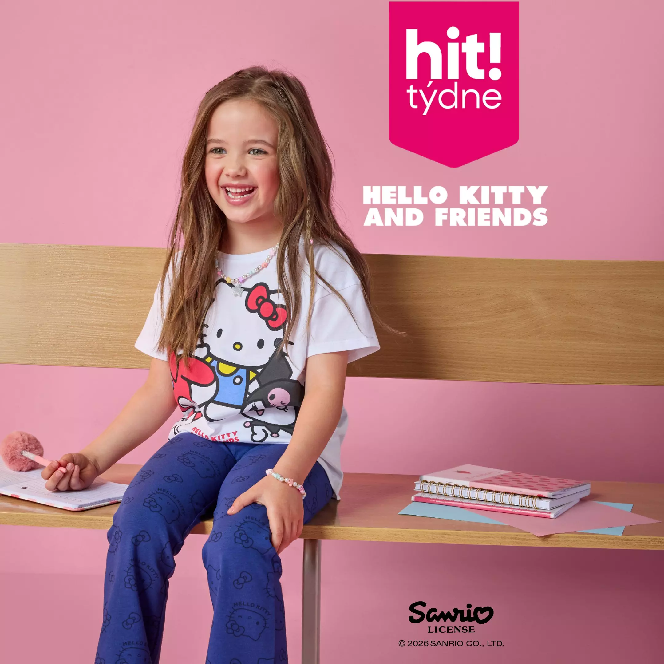 Dívka v Pepco tričku Hello Kitty and Friends sedí na stole s barevnými sešity.