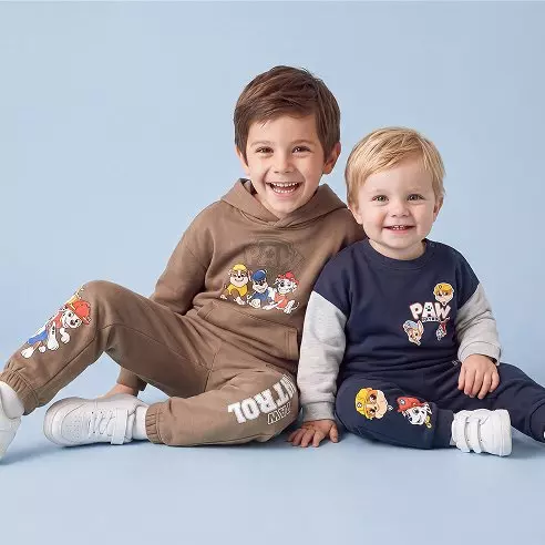 Dos niños sonrientes visten conjuntos de chándal Pepco con estampados de personajes de dibujos animados.