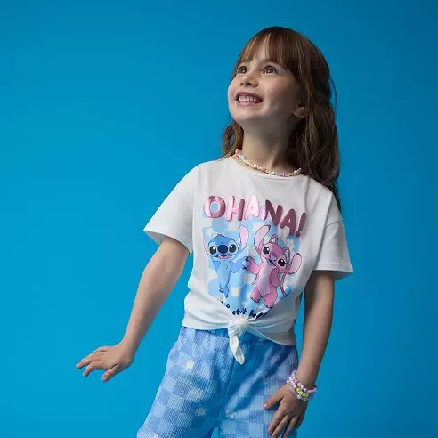 Pepco tricou alb pentru fete cu imprimeu Stitch și text Ohana, purtat cu pantaloni bleu.