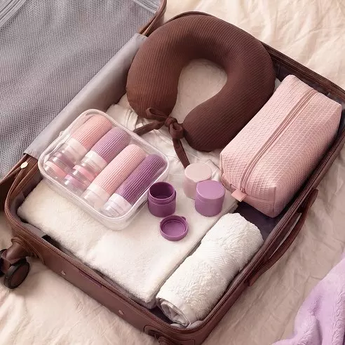 Maleta Pepco marrón organizada con almohada de viaje, toallas, neceser rosa y set de botes de viaje.