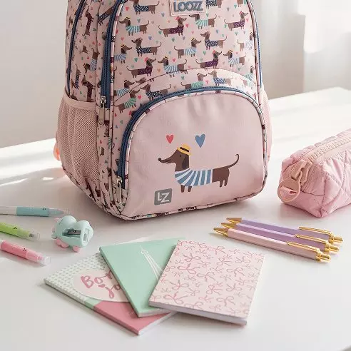 Rucsac roz Pepco cu imprimeu câini și rechizite școlare colorate pe masă.