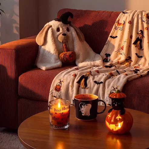 Decorazioni Halloween Pepco su divano con cuscino a forma di fantasma, plaid e zucca illuminata sul tavolino.