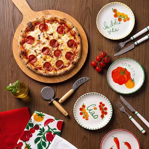 Pepco pizza na dřevěném prkénku s barevnými talíři, příborem a kráječem na pizzu.