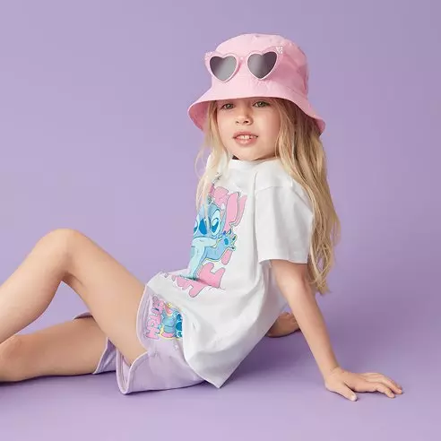 Fetiță purtând tricou alb Pepco cu imprimeu Stitch Disney și pălărie roz cu ochelari de soare.