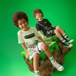 Dos niños sonrientes sentados en un cubo pixelado estilo Minecraft, vistiendo camisetas temáticas del juego.