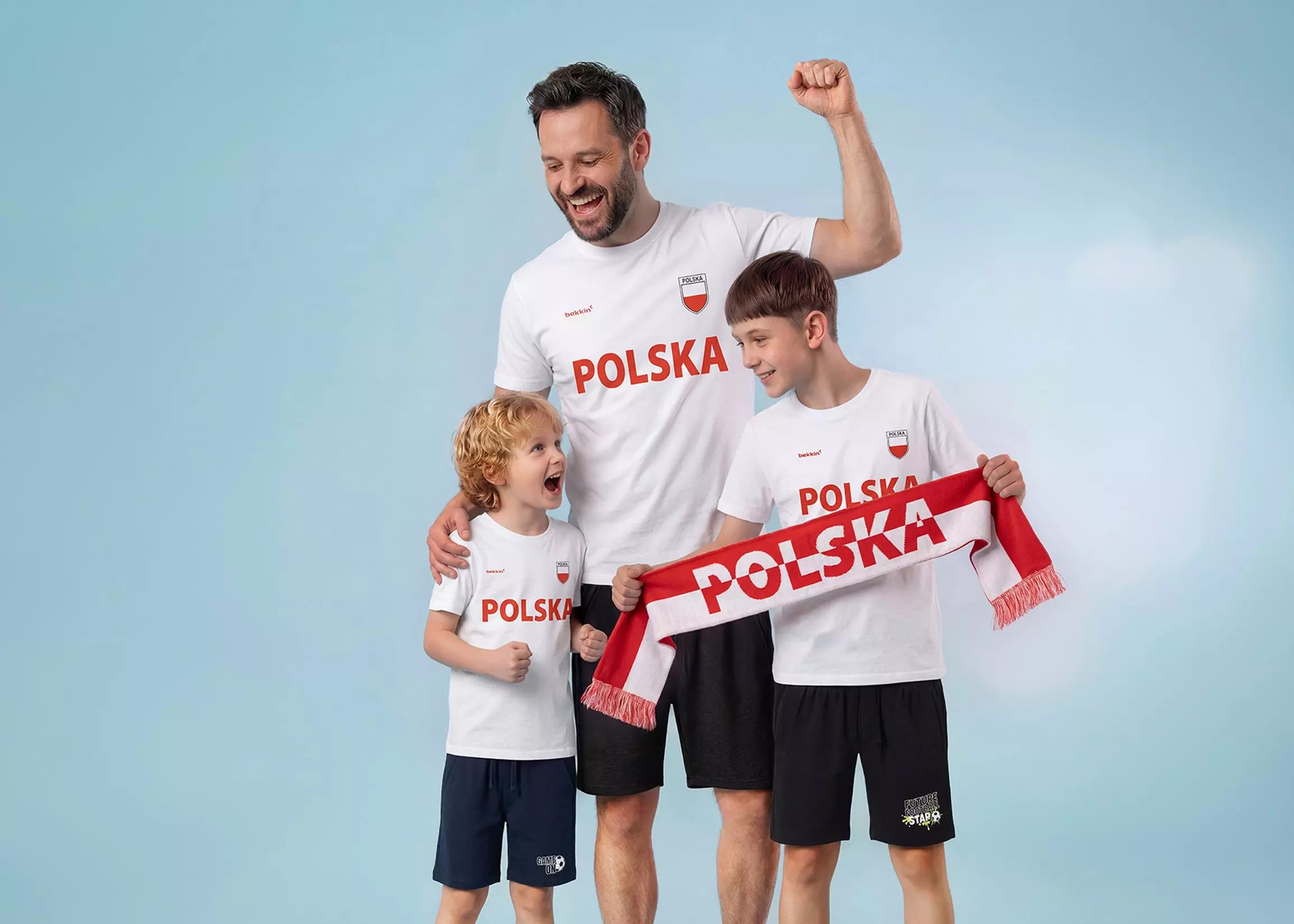 Mężczyzna z dwoma chłopcami w białych koszulkach z napisem POLSKA marki Pepco, trzymający szalik kibica.