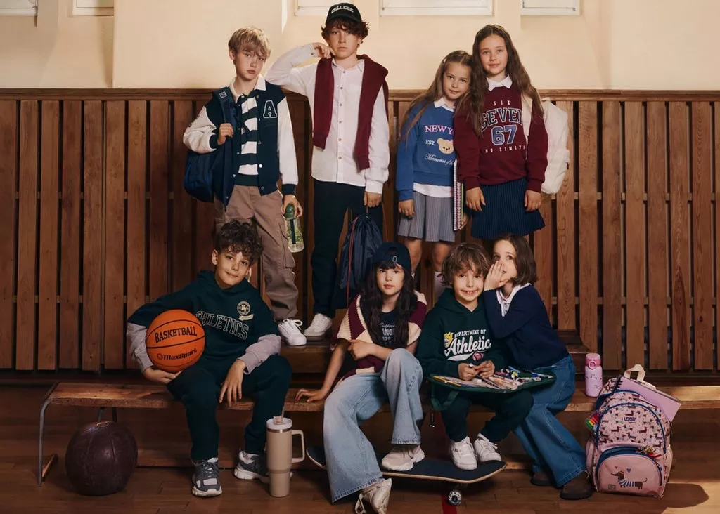 Pepco children wearing casual sportswear including varsity jackets, hoodies and pleated skirts in a school setting.