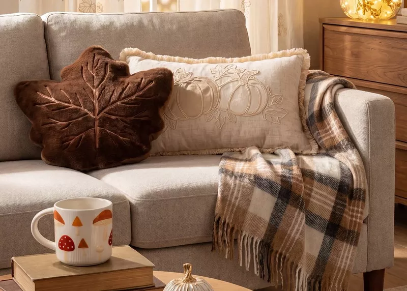 Pepco autumn cushions with leaf and pumpkin designs on a beige sofa with checked throw and seasonal mug.
