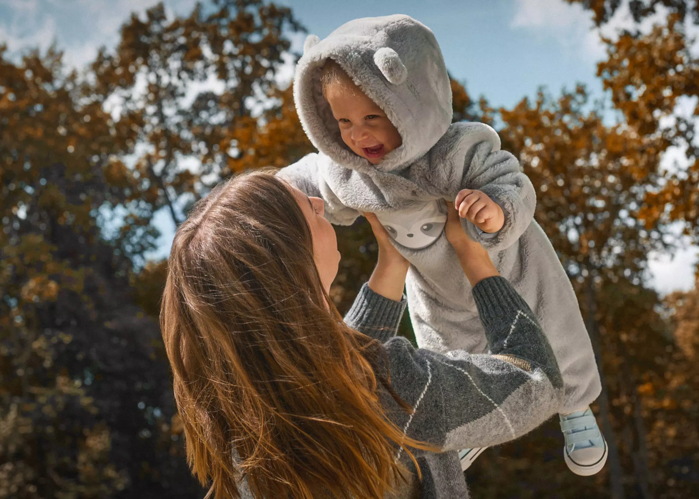 Mamma solleva bambino che indossa tuta grigia con cappuccio a orecchie Pepco all'aperto.