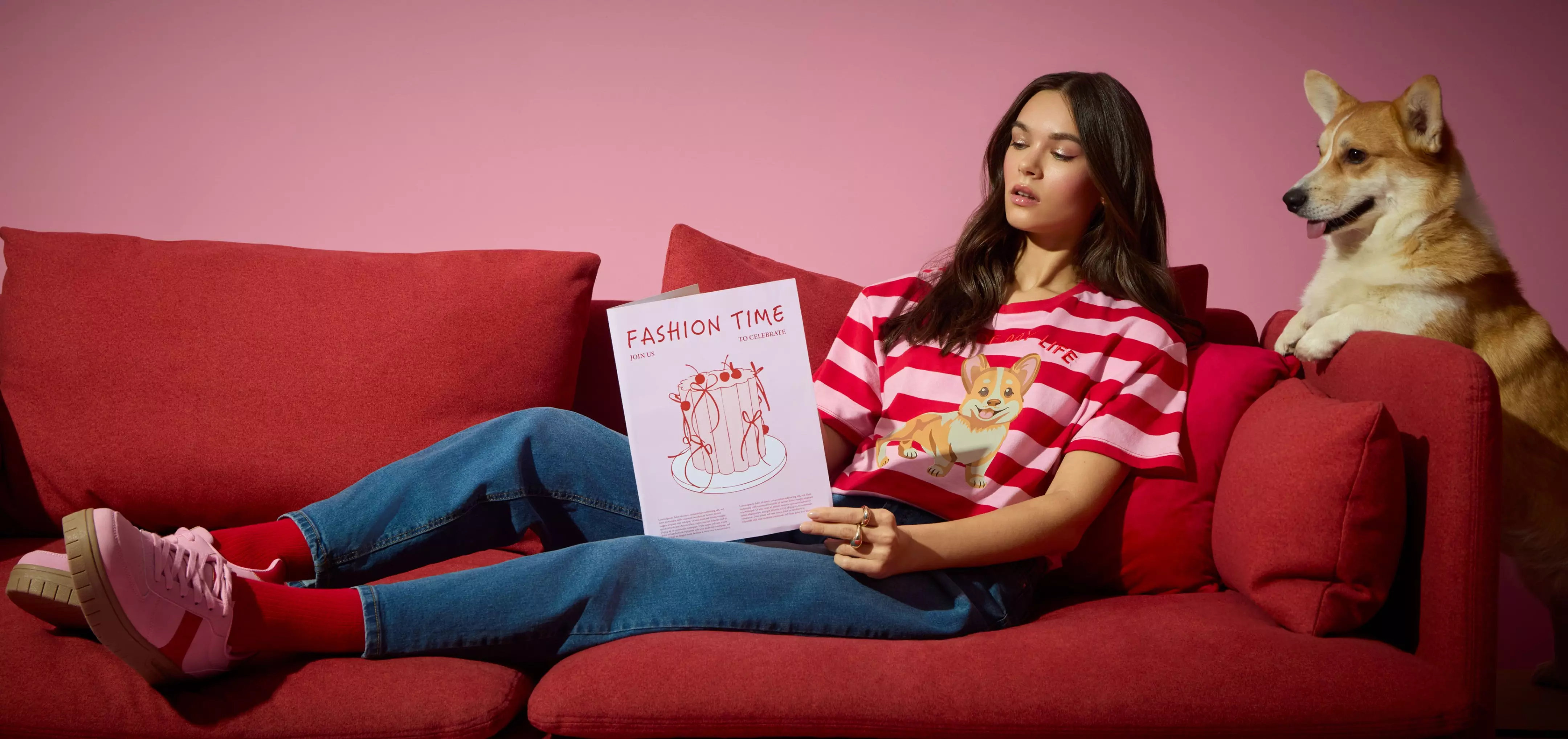 Osoba w pasiastej koszulce Pepco z nadrukiem corgi, czytająca magazyn na czerwonej kanapie obok prawdziwego psa corgi.