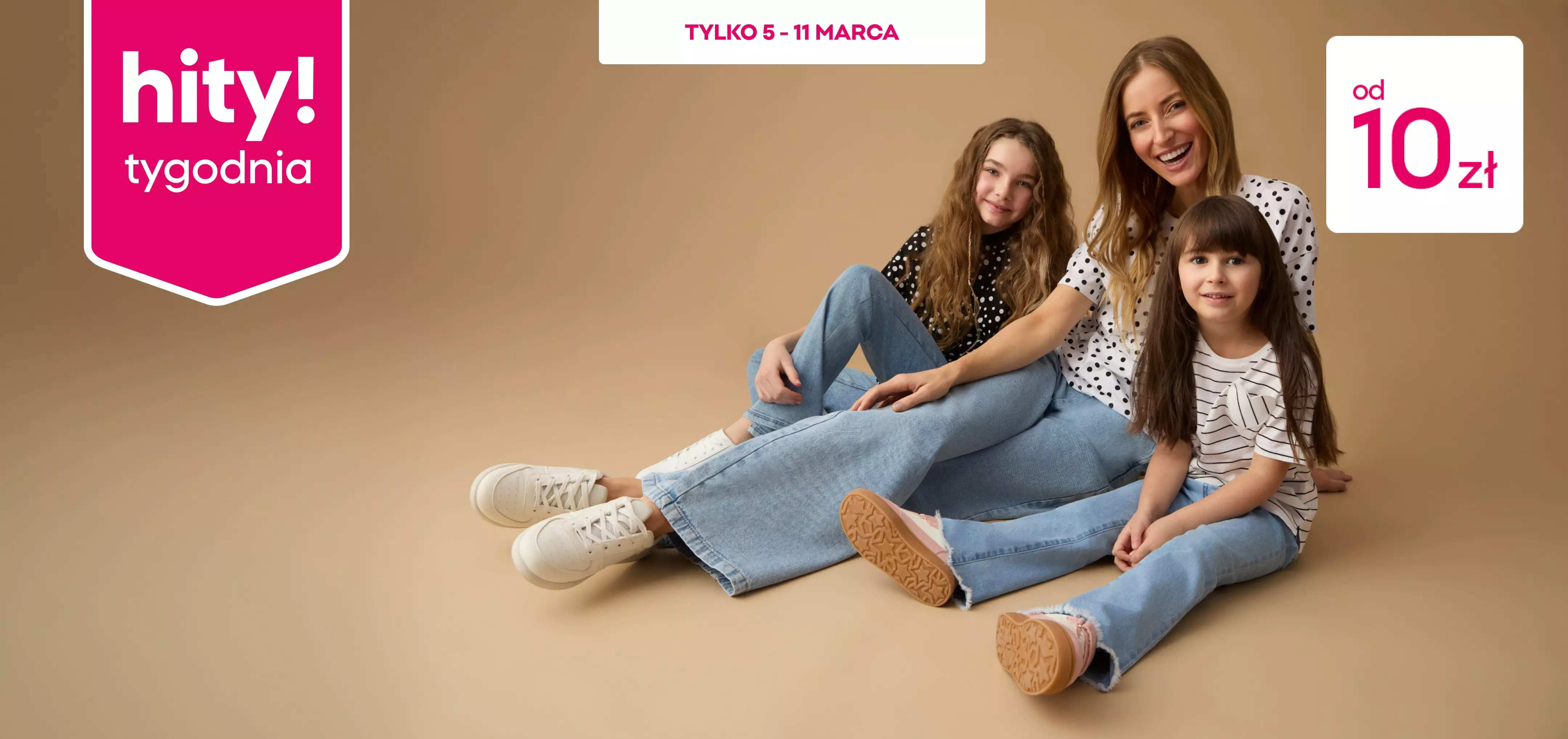 Matka z dwiema córkami siedzi na podłodze, ubrane w dżinsy i bluzki w kropki i paski.