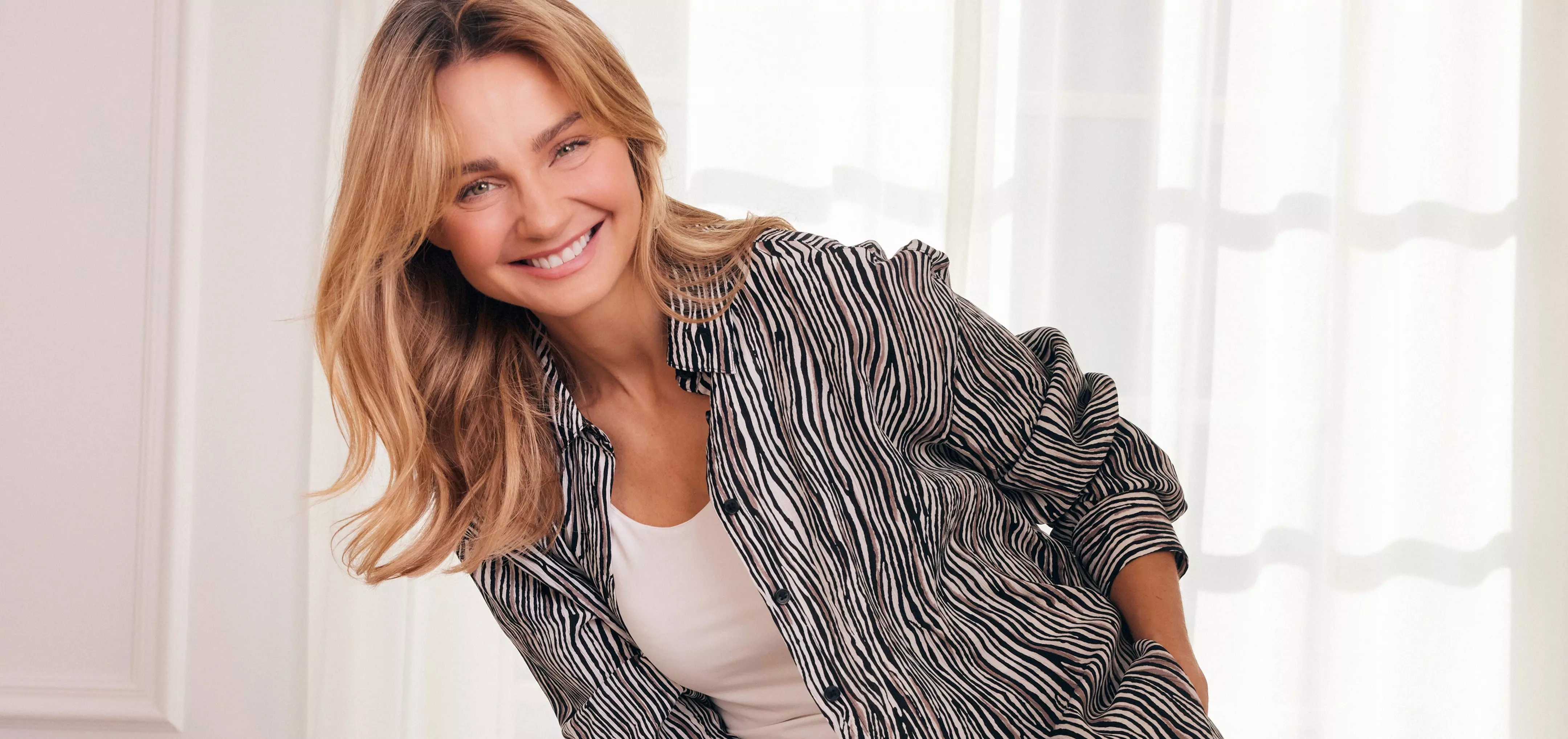 Woman smiling wearing a black and white striped blazer over a white top.