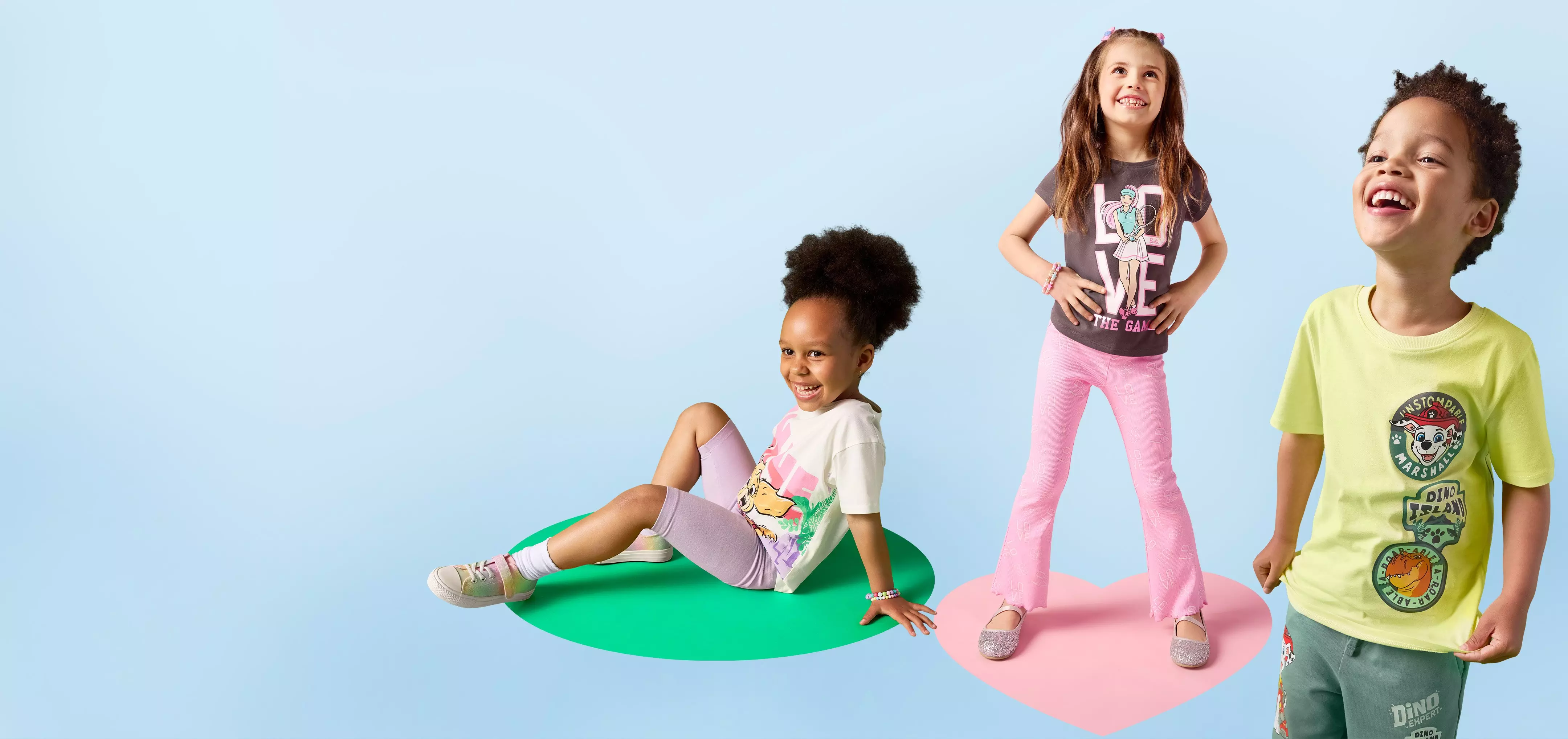 Tres niños sonrientes luciendo camisetas y pantalones coloridos de la colección infantil Pepco.