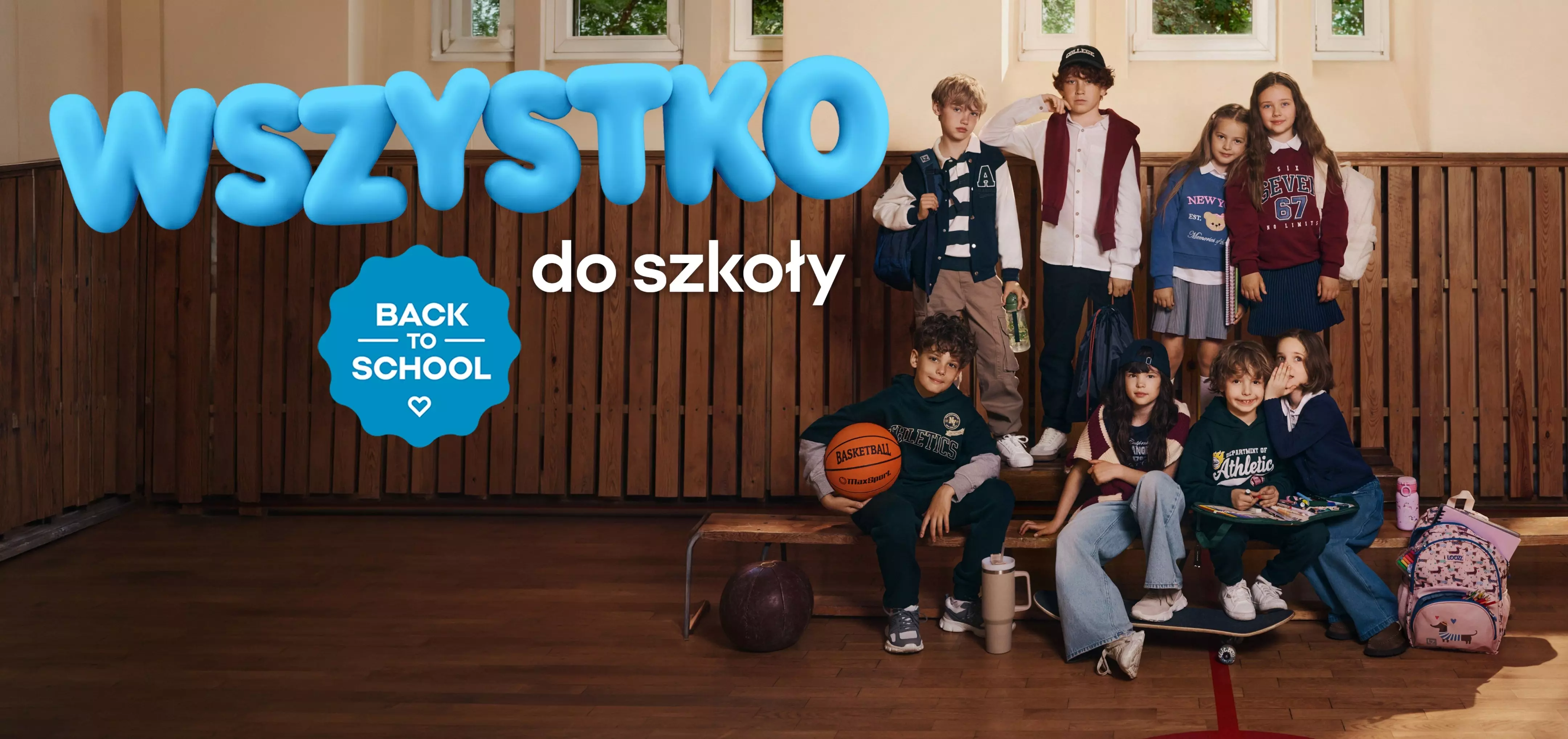 Grupa dzieci w szkolnych strojach Pepco z napisem WSZYSTKO do szkoły BACK TO SCHOOL w sali gimnastycznej.