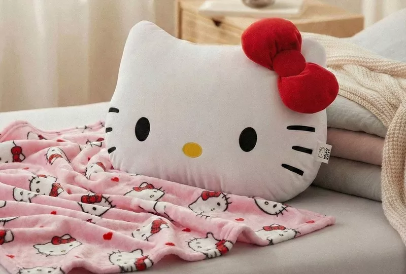 Poduszka Hello Kitty z czerwoną kokardką od Pepco na łóżku z różowym kocem w ten sam wzór.
