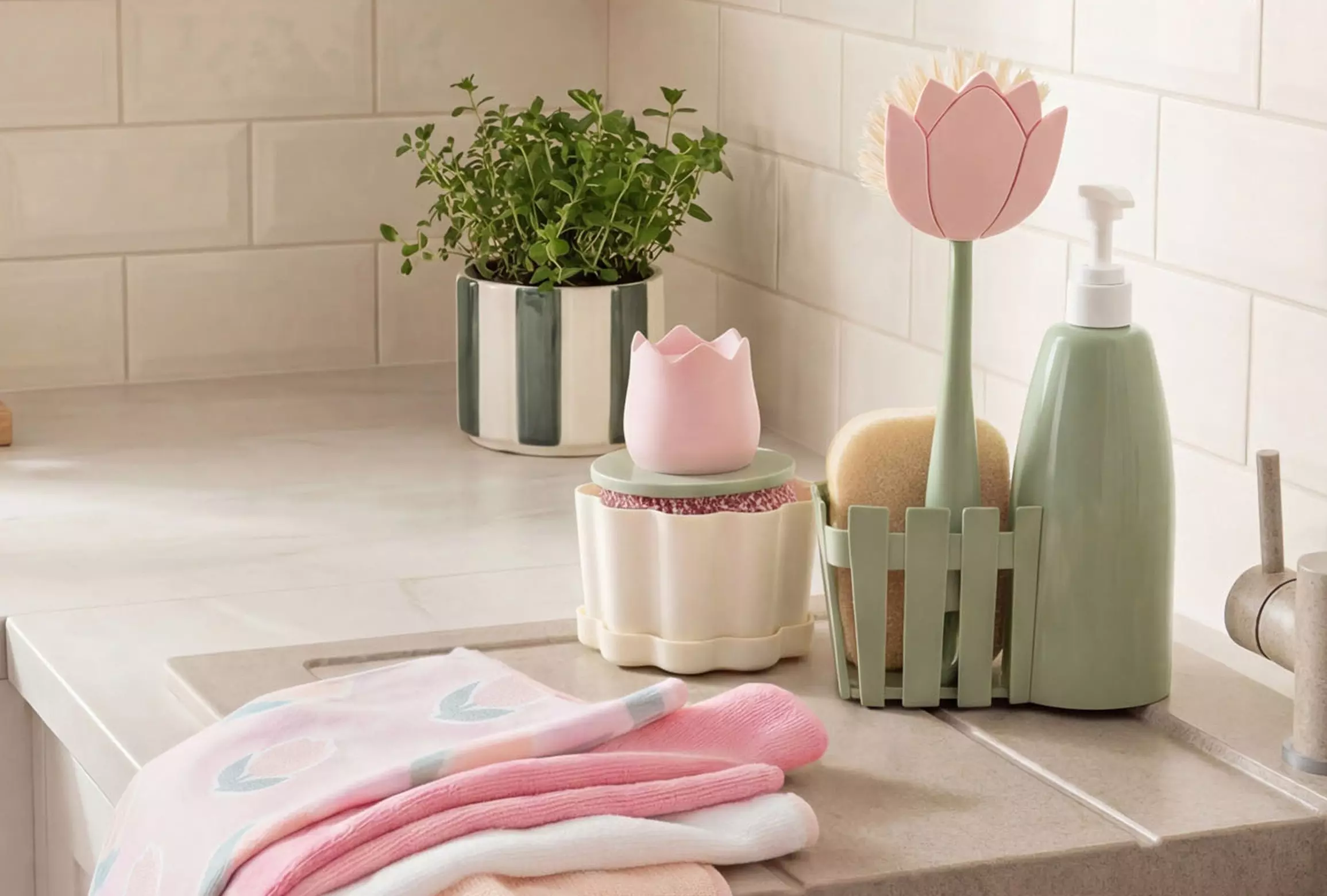 Zestaw łazienkowy z różowymi i zielonymi dekoracjami, dozownikiem mydła w kształcie tulipana, doniczką z ziołami i złożonymi ręcznikami.