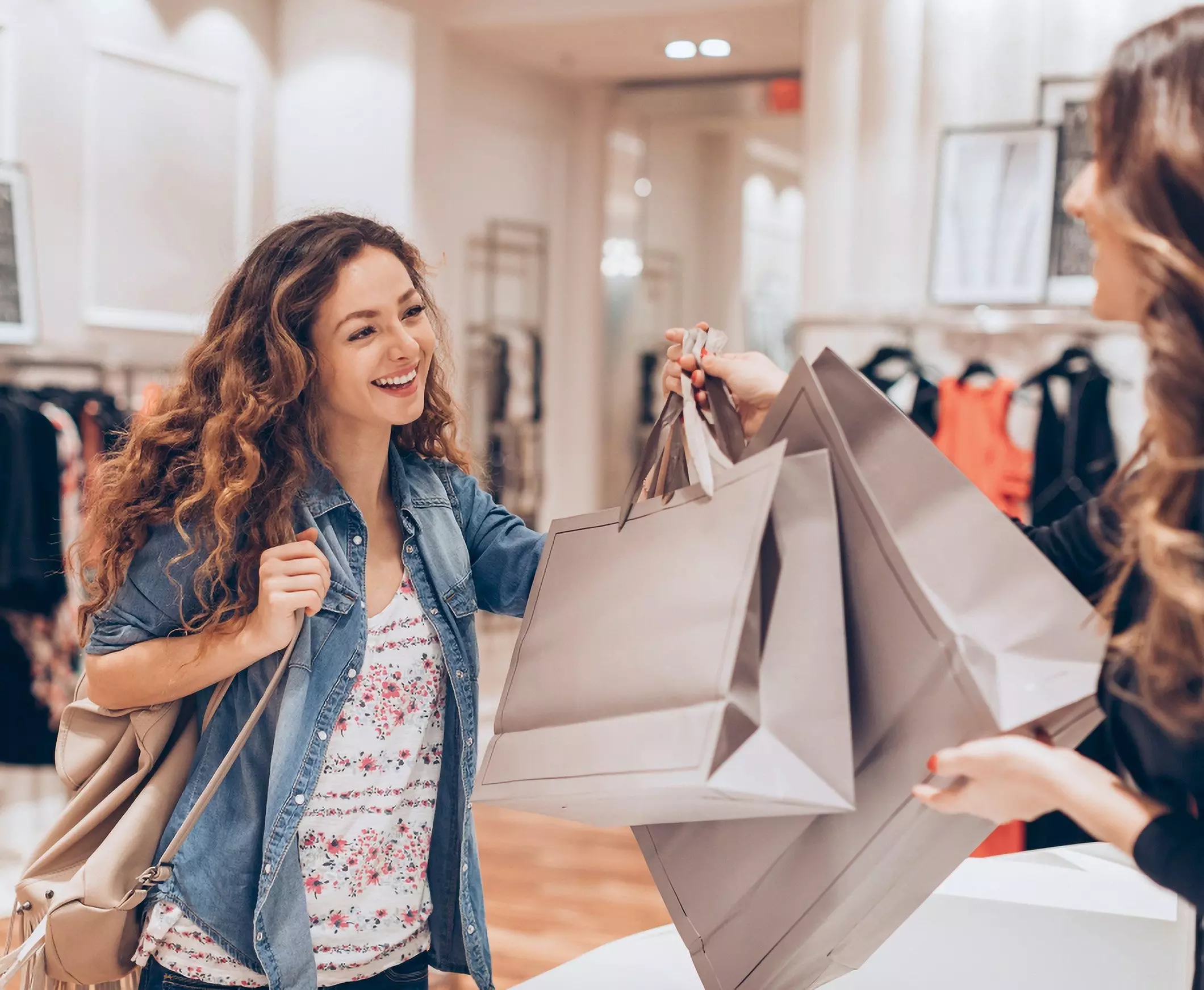 Clientă primind mai multe pungi de cumpărături în magazinul Pepco, purtând o jachetă din denim peste o bluză cu model floral.