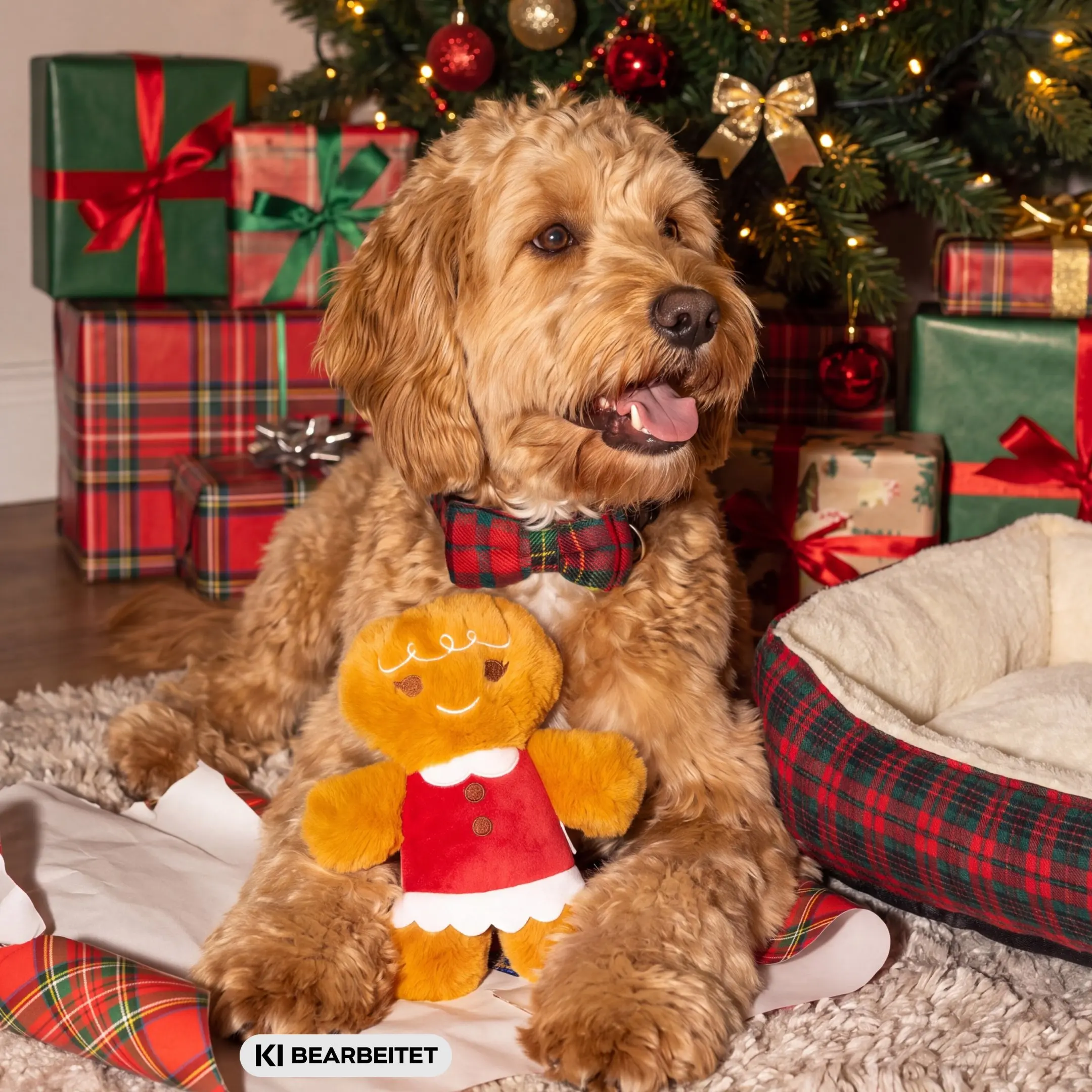 Pepco Hund mit Fliege hält Lebkuchen-Plüschtier vor Weihnachtsbaum und Geschenken, Text KI BEARBEITET.