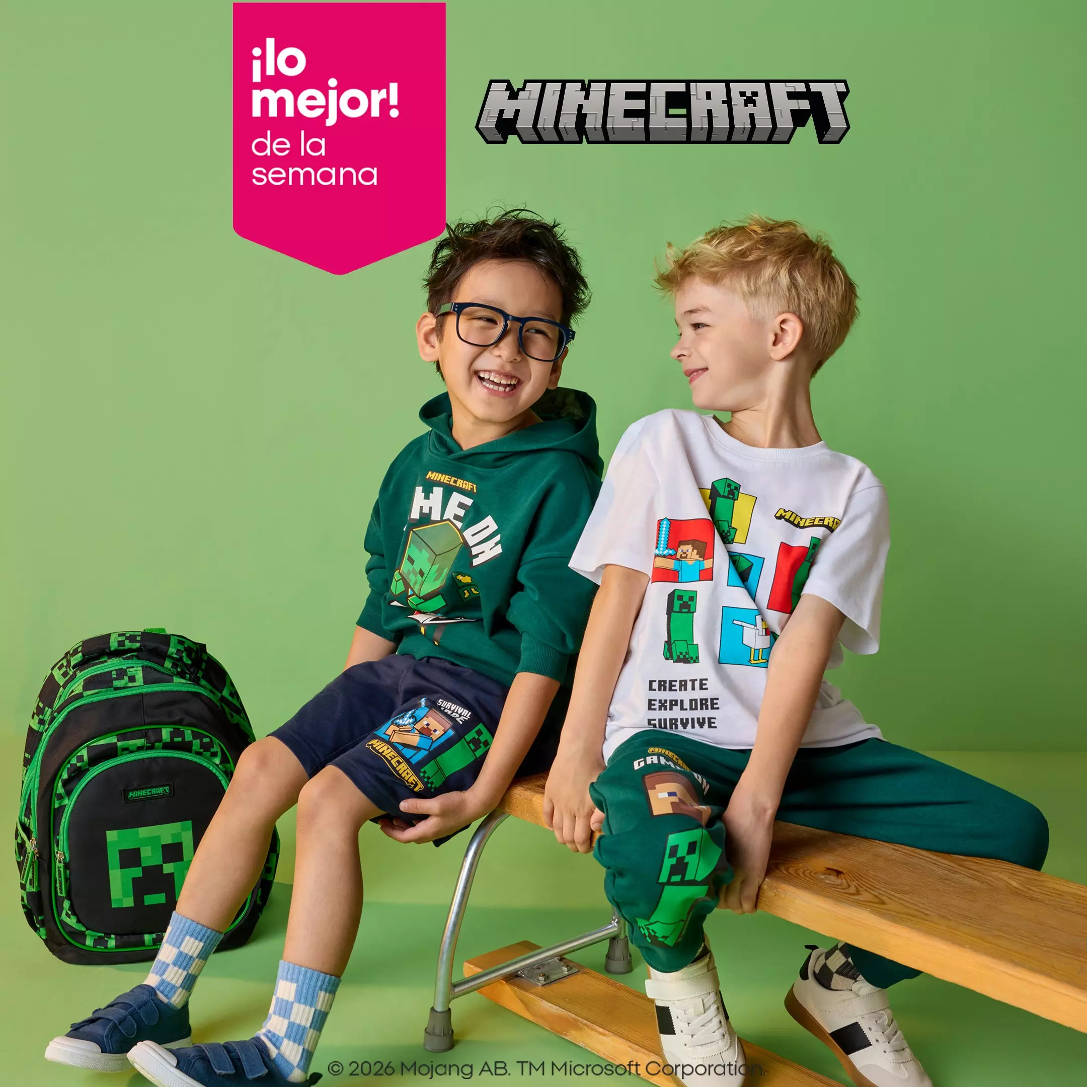Dos niños sonrientes visten ropa de Minecraft de Pepco, sentados junto a una mochila con diseño de Creeper.
