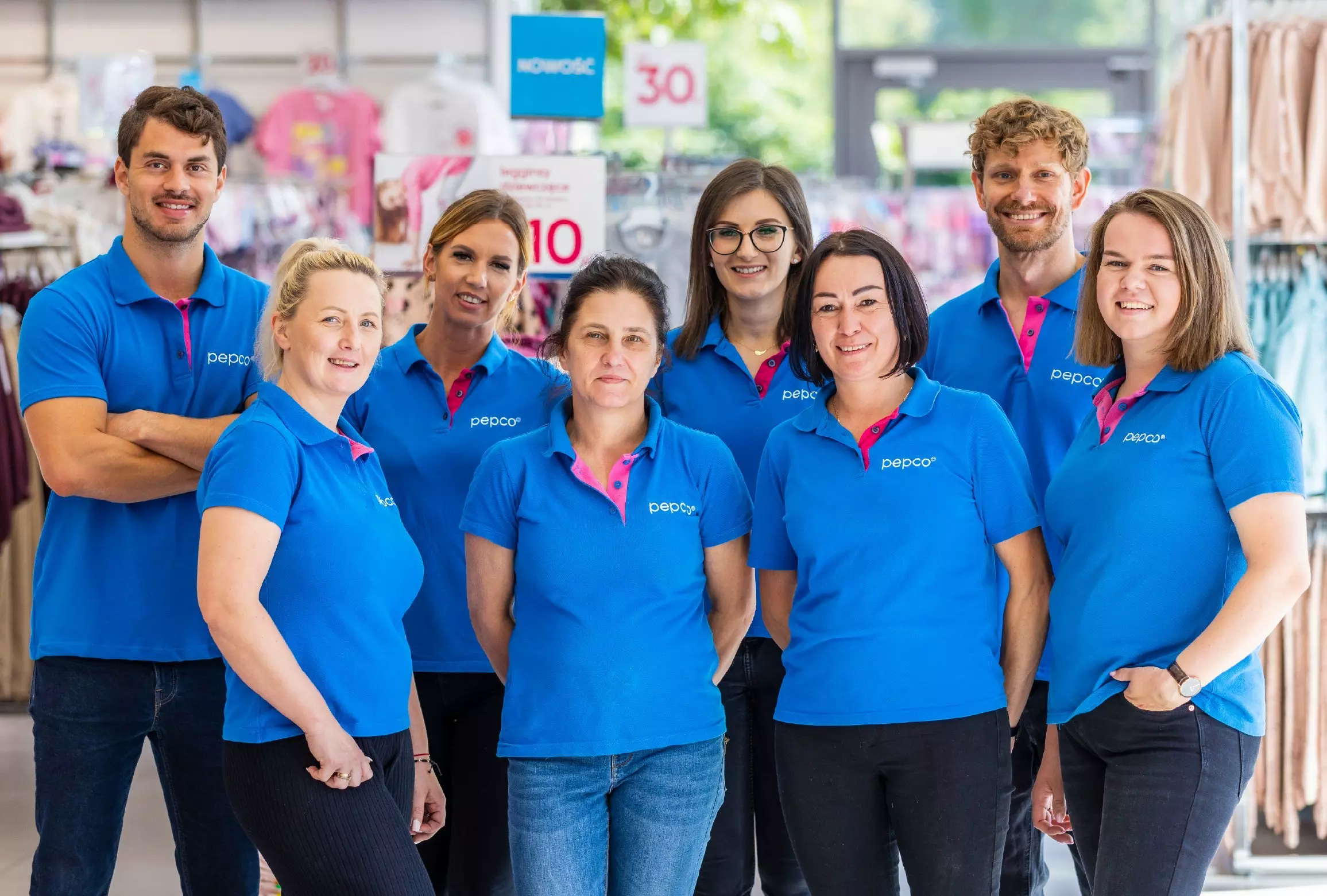 Echipă de opt angajați Pepco purtând tricouri polo albastre, zâmbind în magazin.