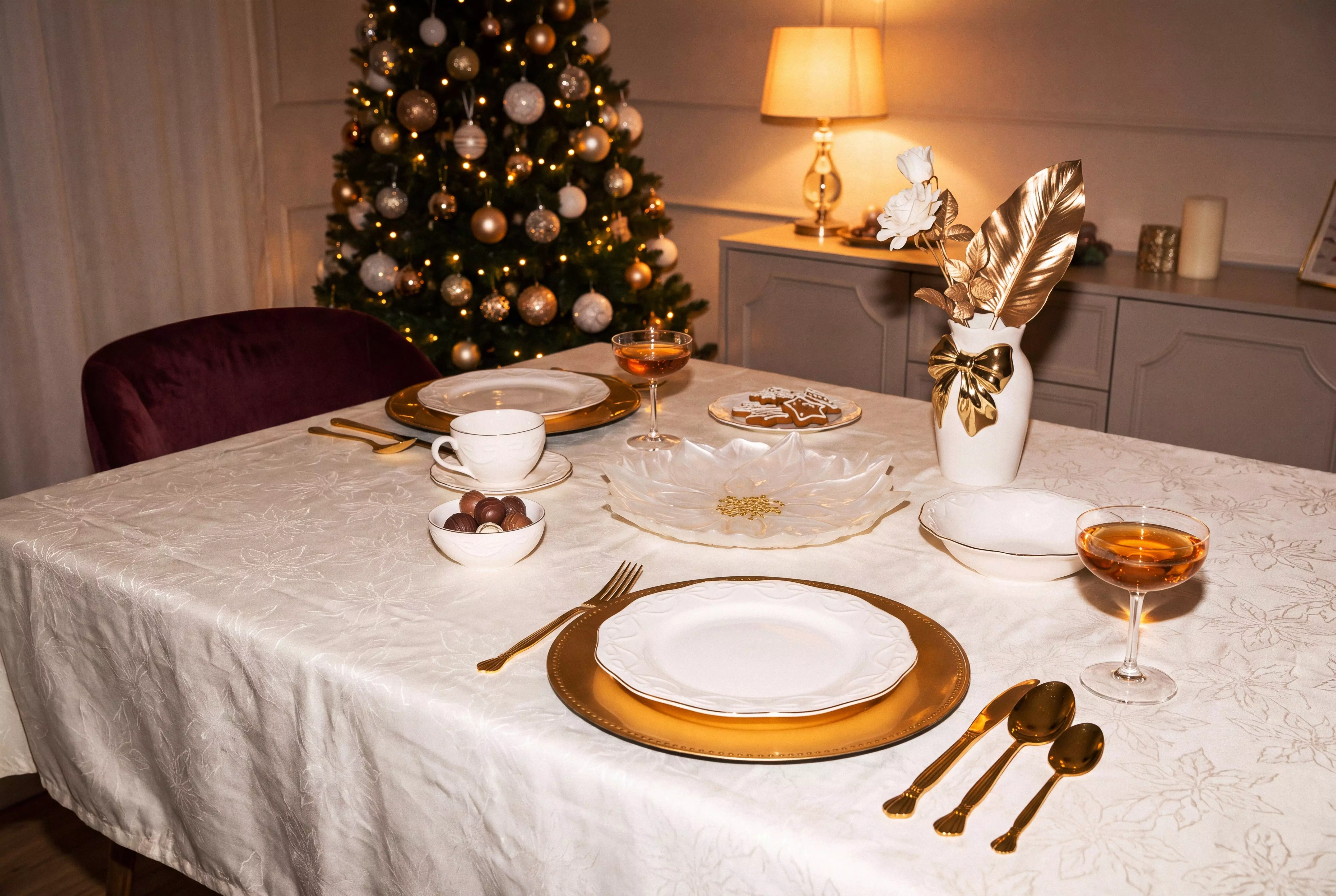 Pepco festive dining table set with white and gold tableware, decorative vase, and illuminated Christmas tree.