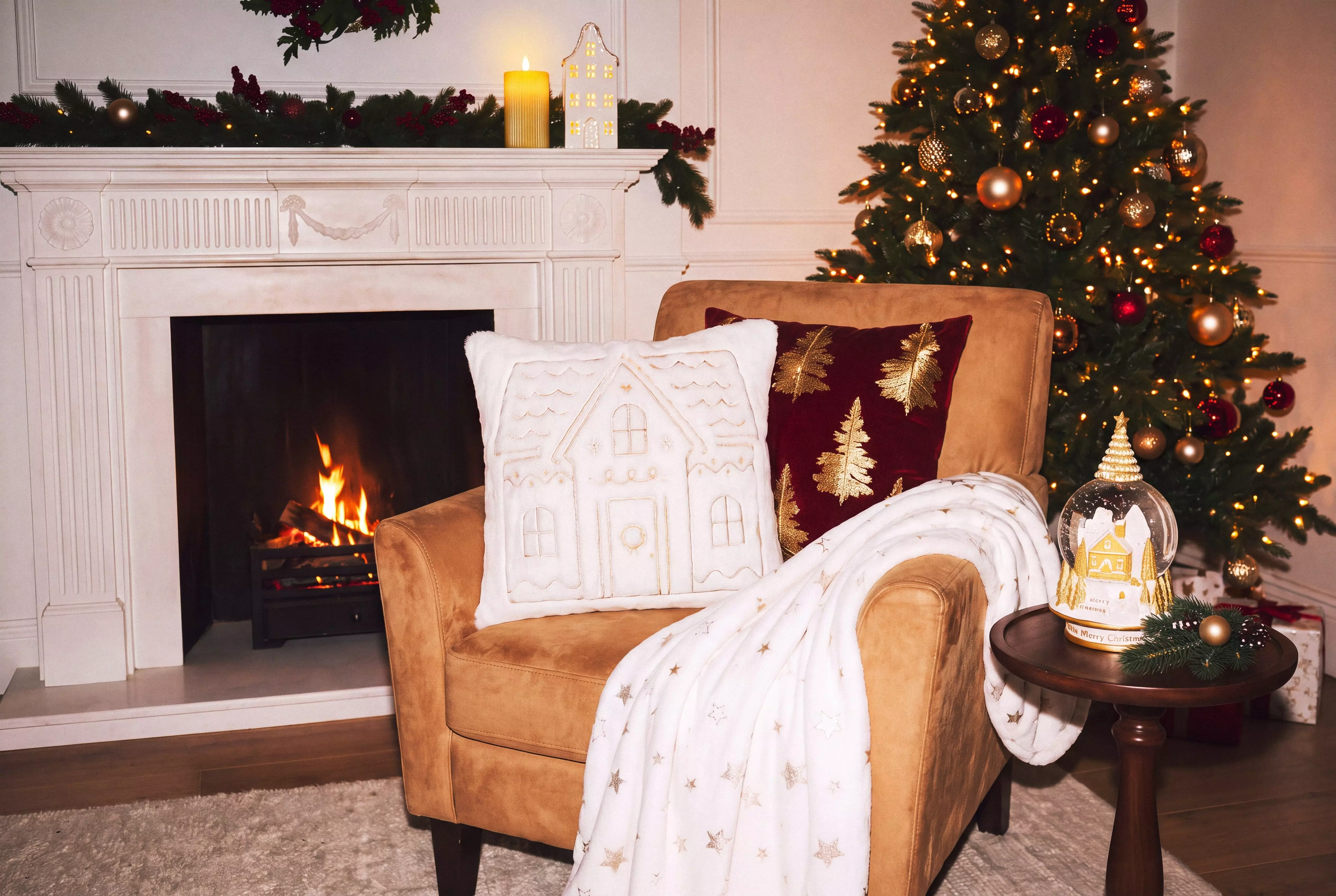 Pepco Christmas living room with armchair displaying festive cushions and throw beside fireplace and decorated tree.