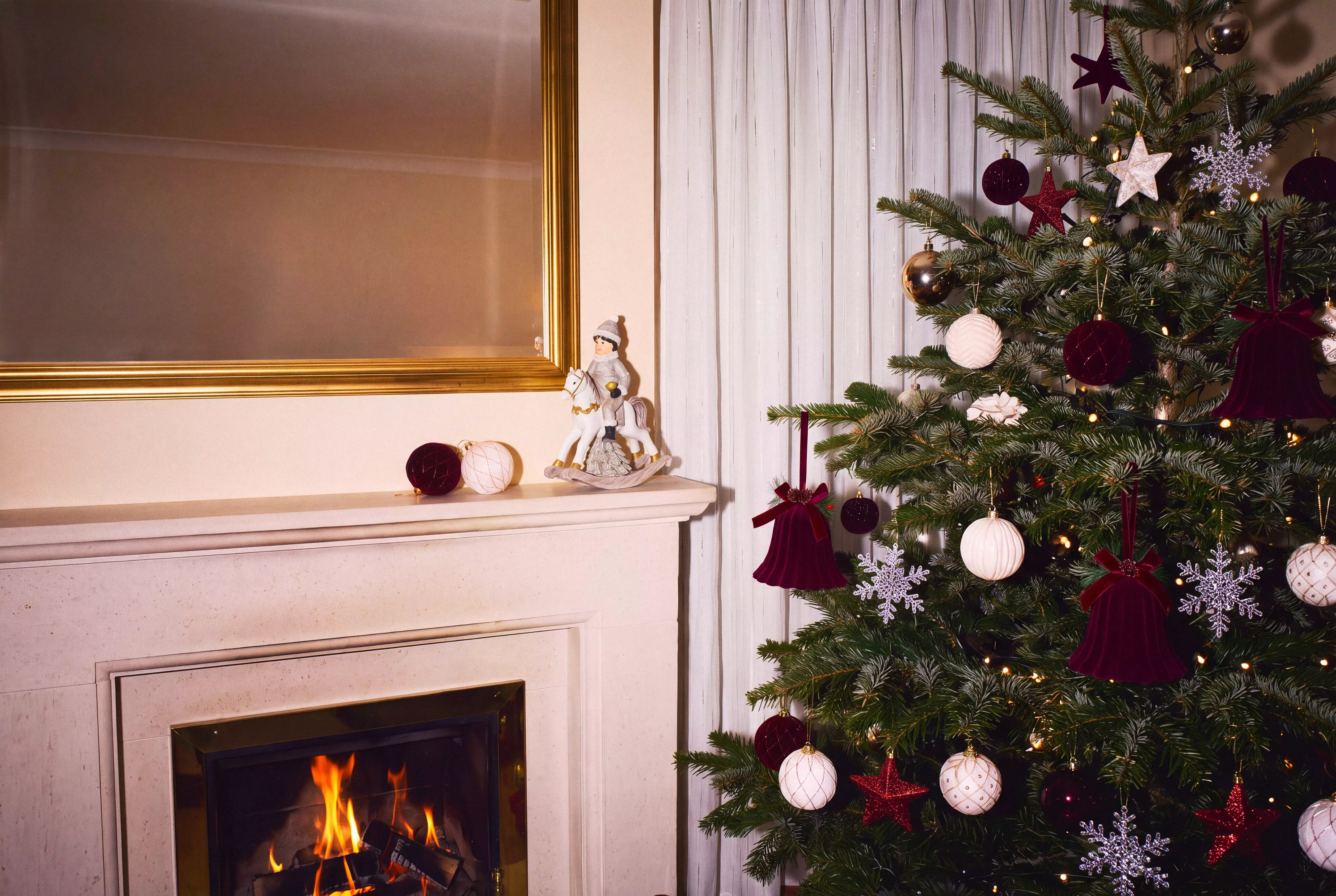 Pepco Christmas tree decorated with burgundy and white baubles, stars and snowflakes beside a lit fireplace.