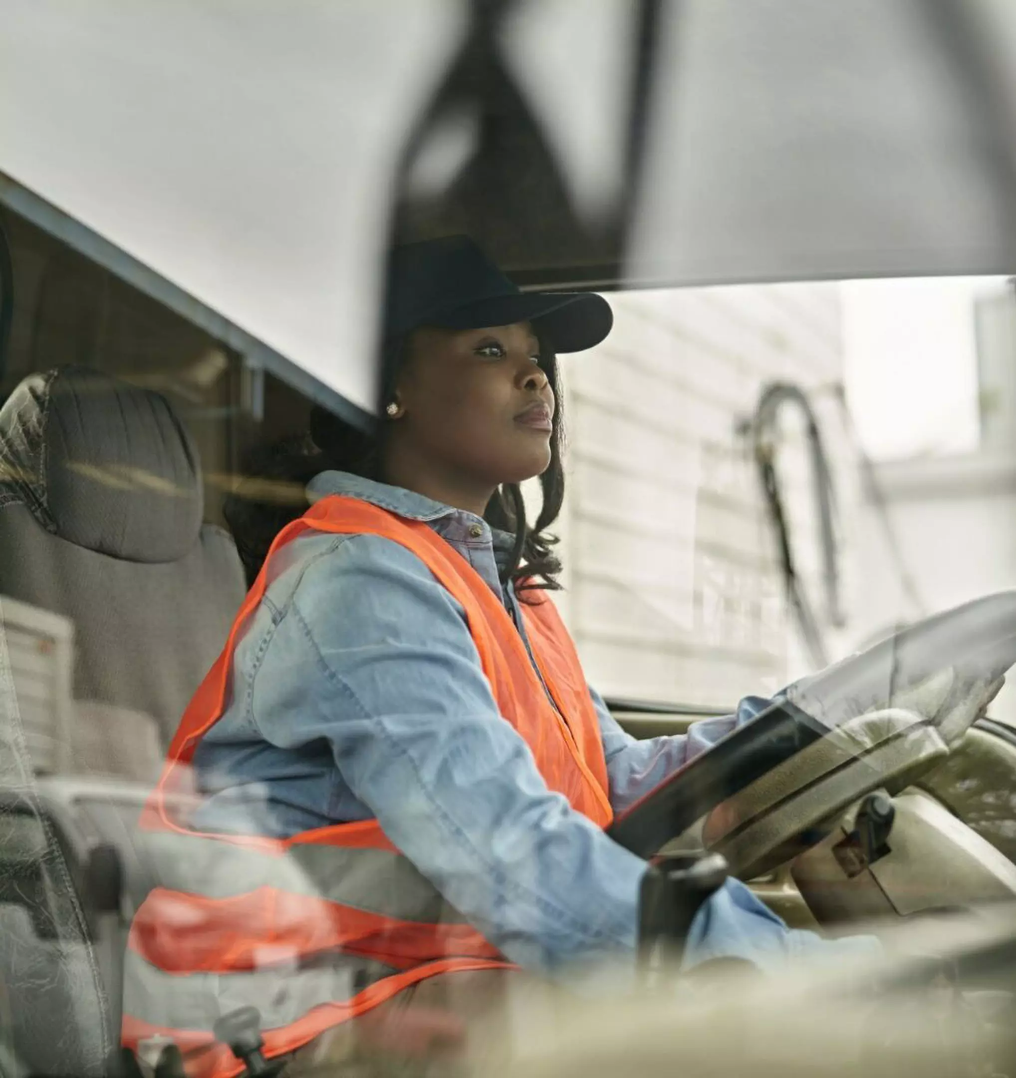 Person wearing Pepco safety vest and cap driving a vehicle, viewed through the windshield.