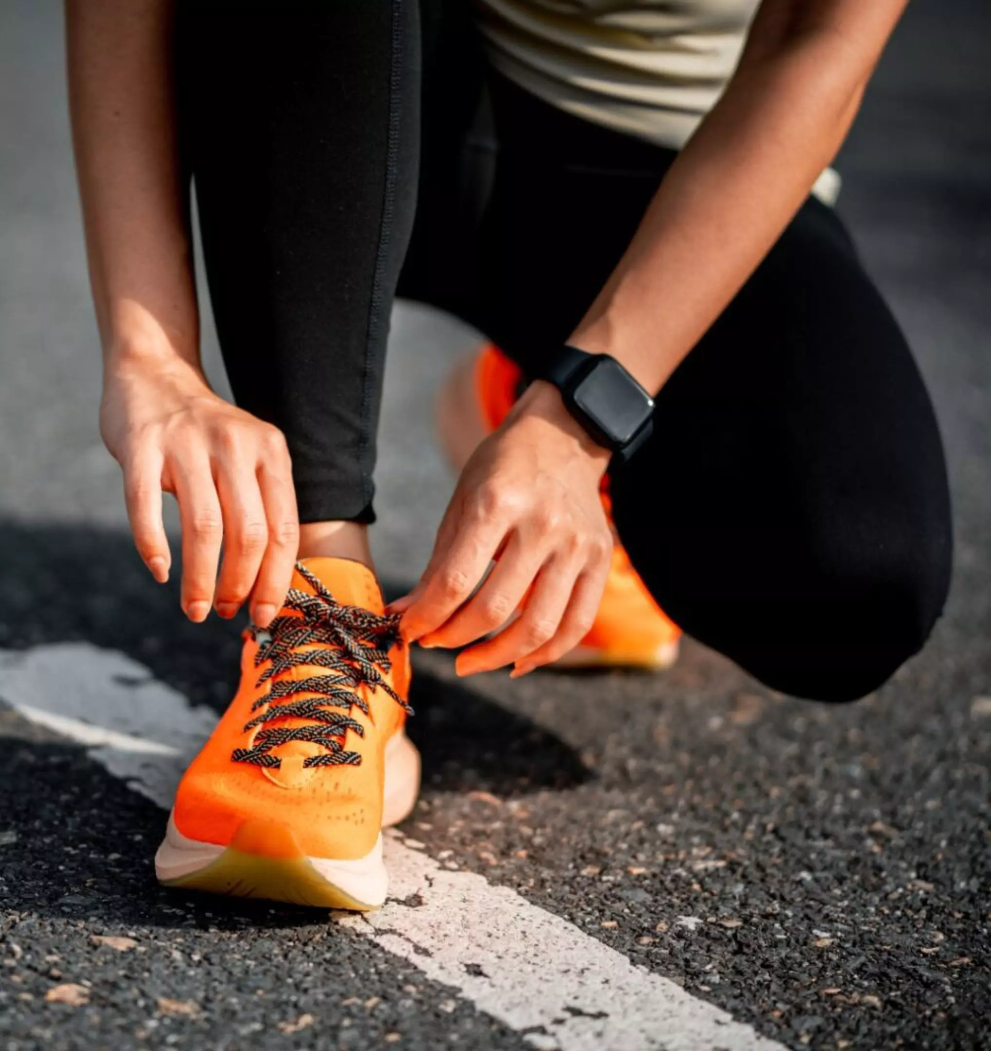 Person tying bright orange Pepco running shoes, wearing black leggings and a fitness watch on their wrist.