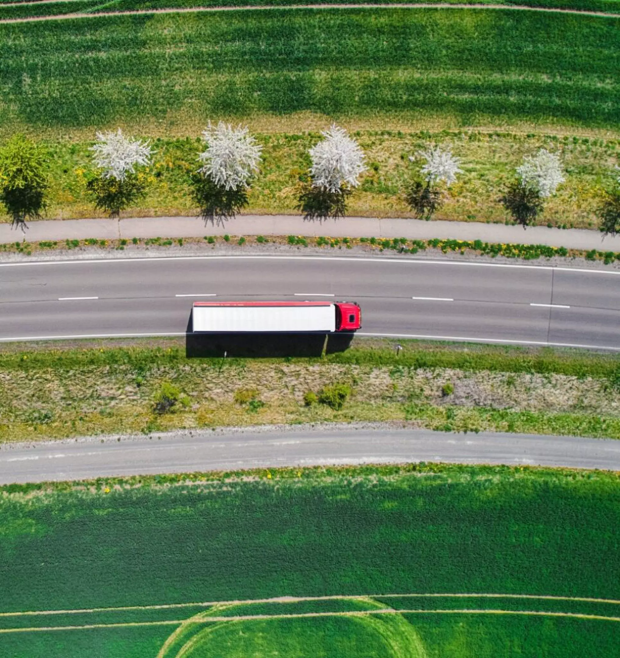 Aerial view of a Pepco delivery truck traveling on a highway bordered by flowering trees and green agricultural fields.
