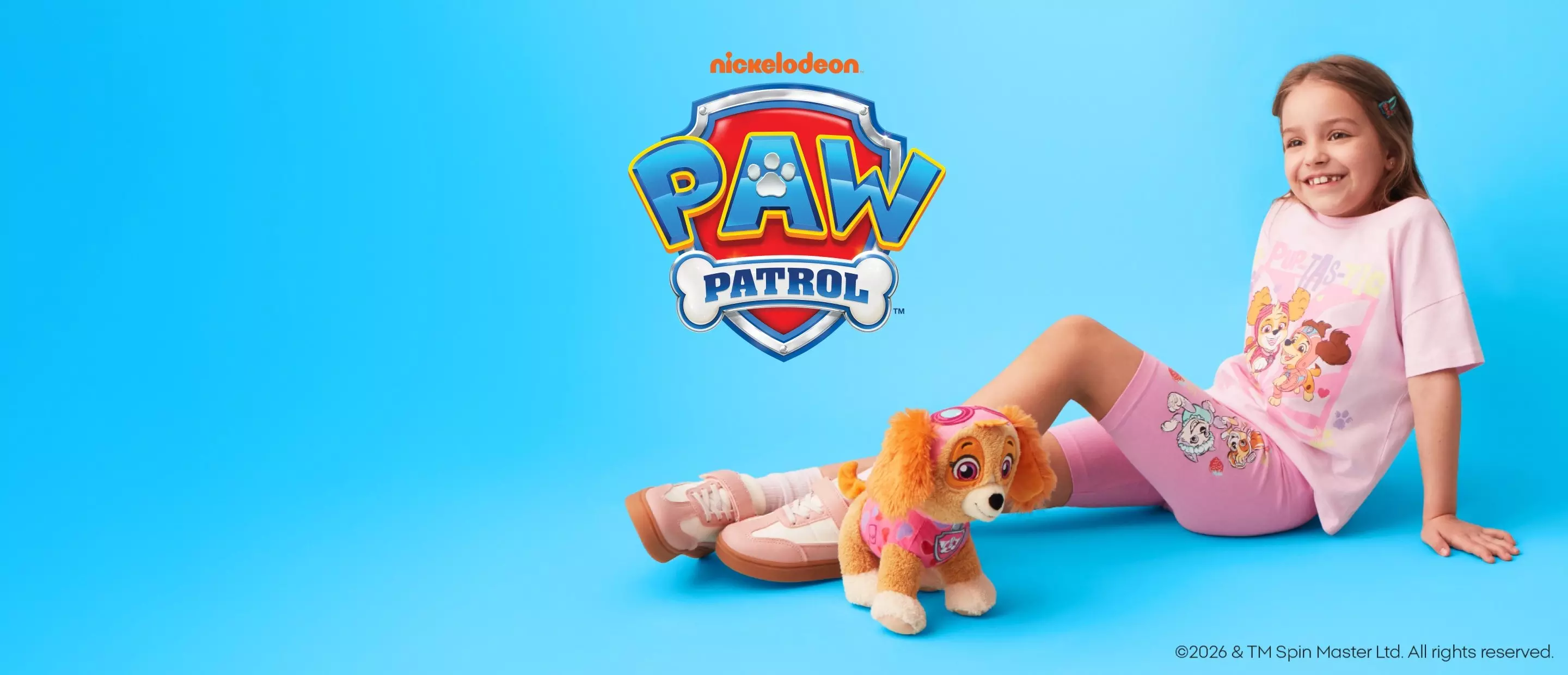 Dziewczynka w różowej piżamie Psi Patrol siedzi z pluszowym psem na tle logo Nickelodeon.