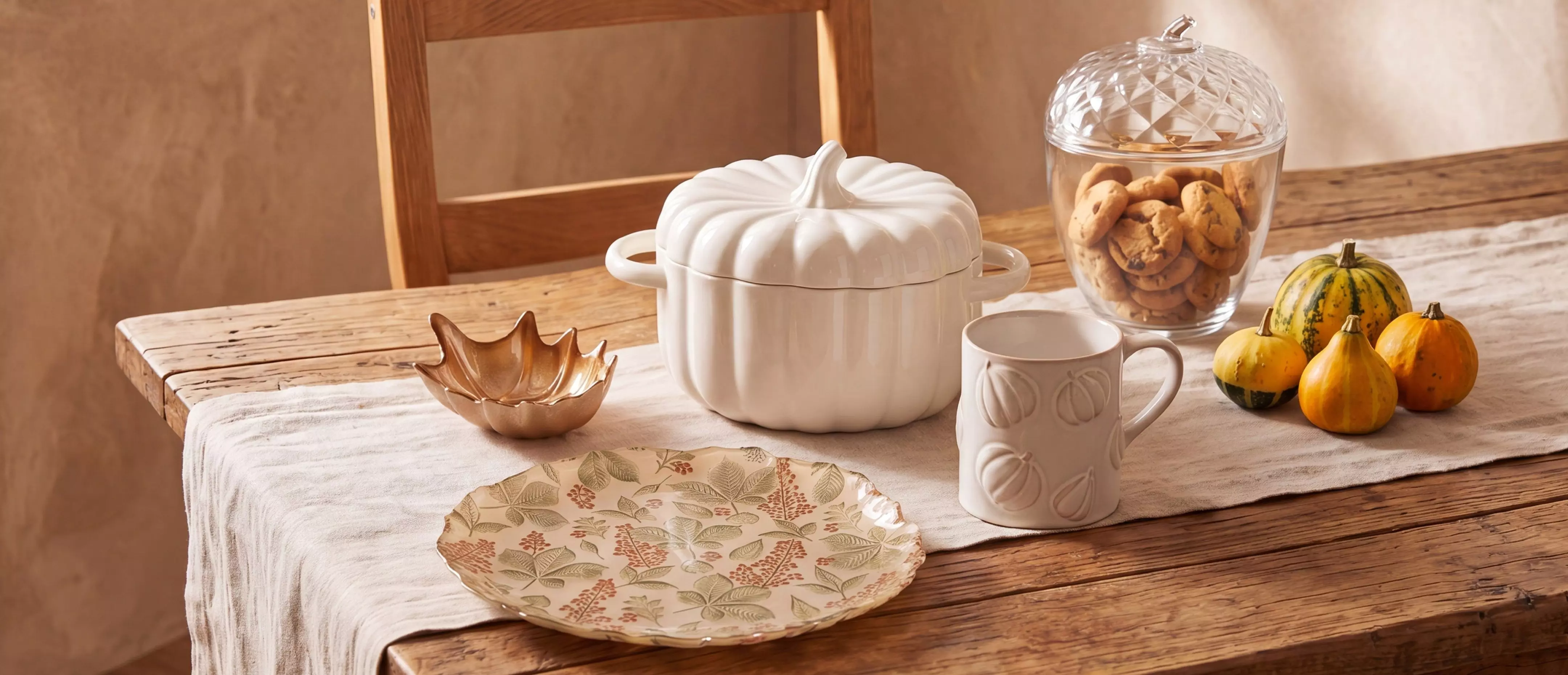 Coleção de decoração outonal Pepco com terrina em forma de abóbora, caneca, pratos e mini abóboras decorativas.