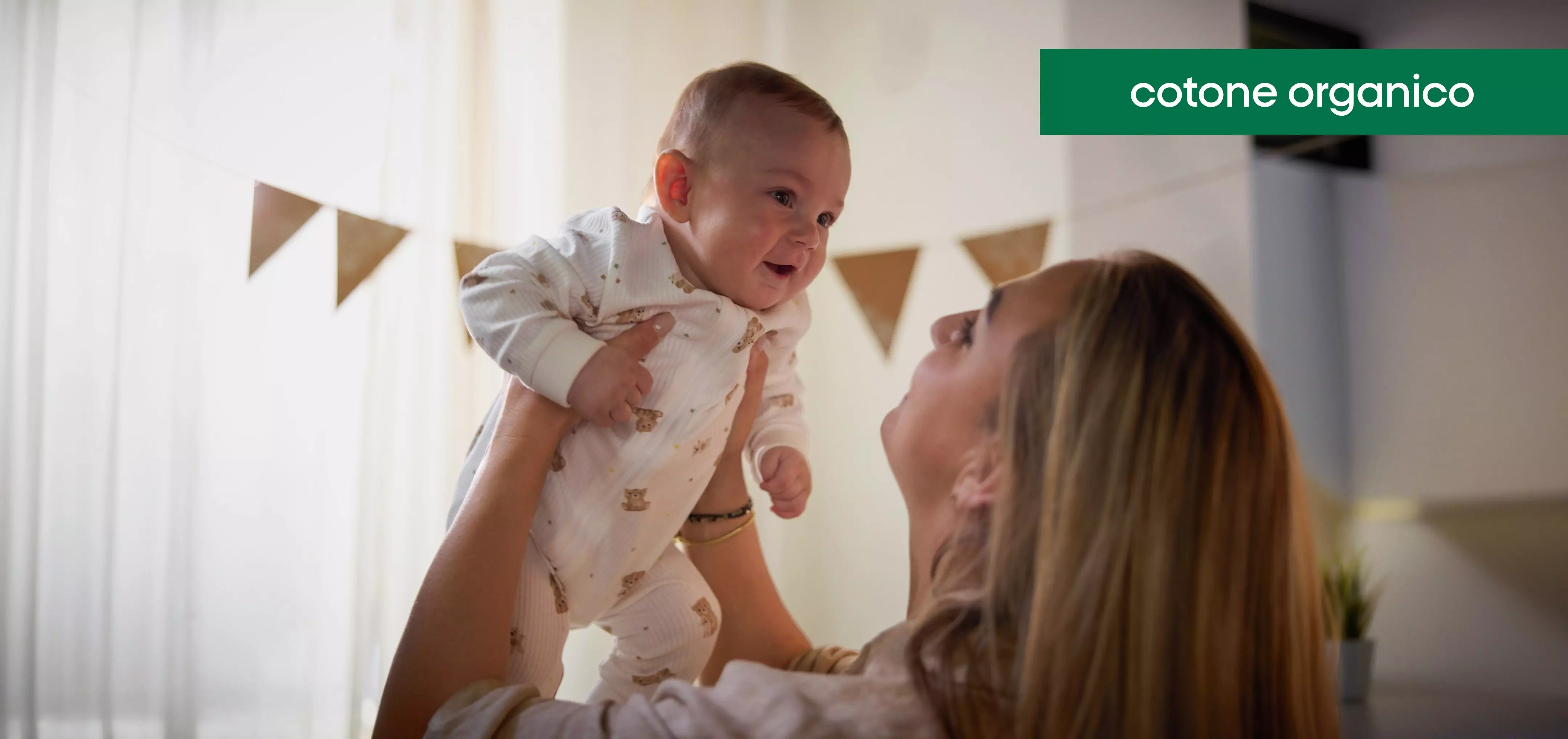 Mamma solleva un neonato sorridente che indossa un pigiama in cotone organico Pepco con stampa di orsetti.