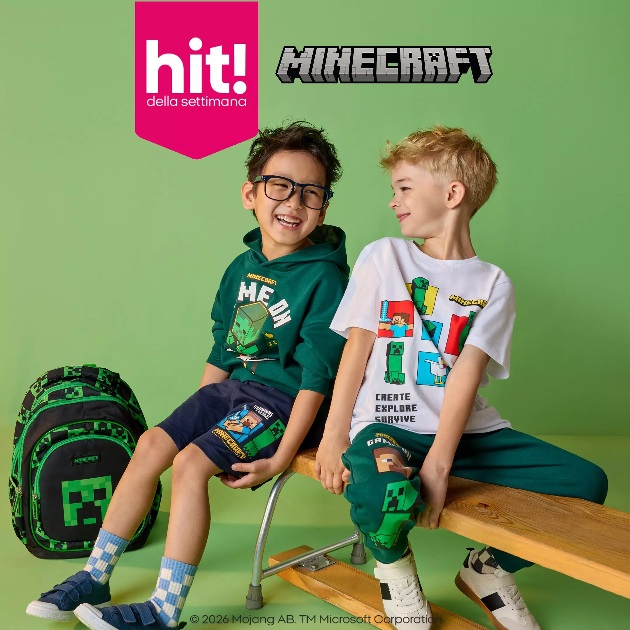 Due bambini sorridenti indossano abbigliamento Minecraft di Pepco, seduti su una panchina con uno zaino.