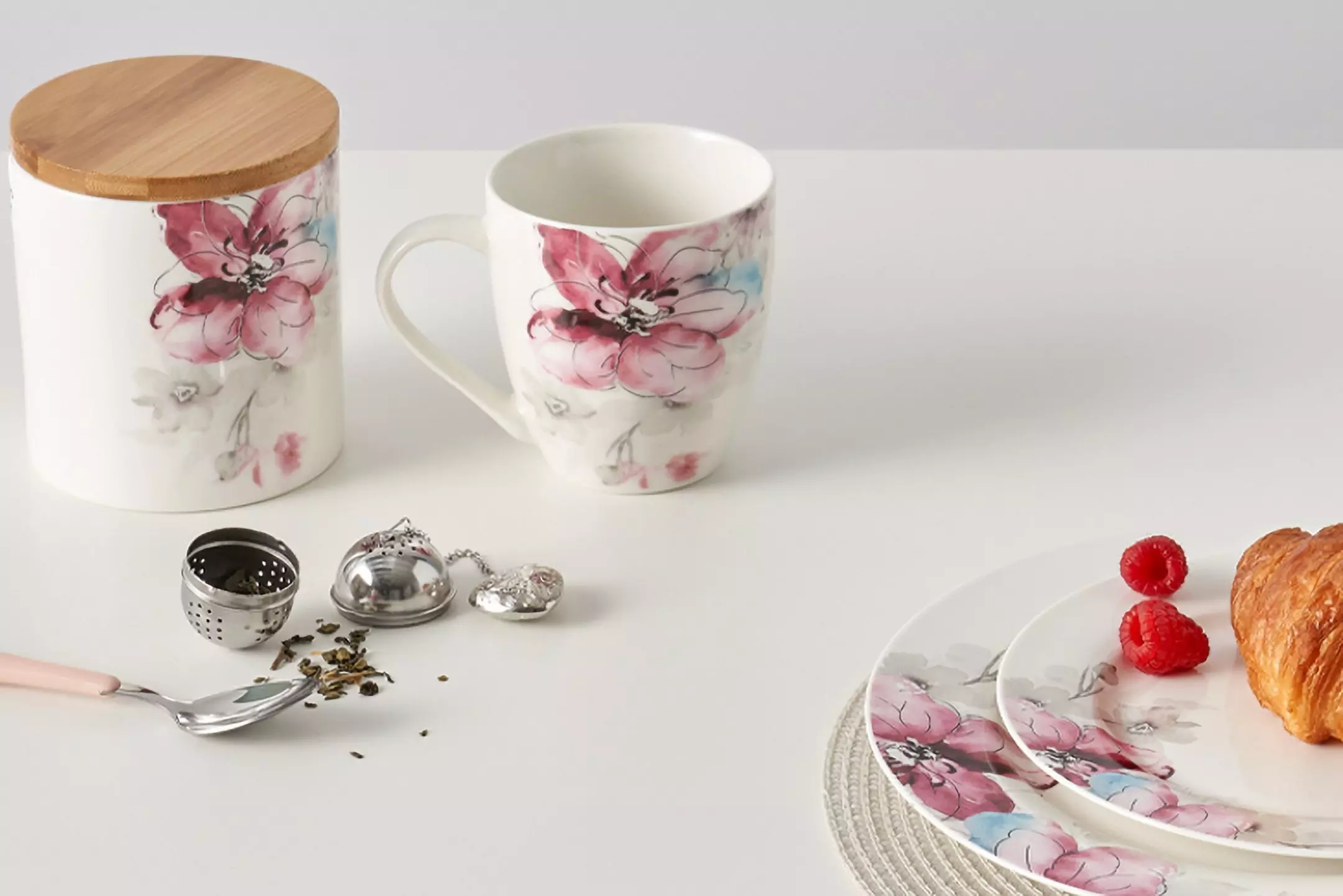 Porcelanowy zestaw śniadaniowy Pepco z kwiatowym wzorem, zawierający kubek, pojemnik z drewnianą pokrywką i talerzyki z rogalikiem i malinami.