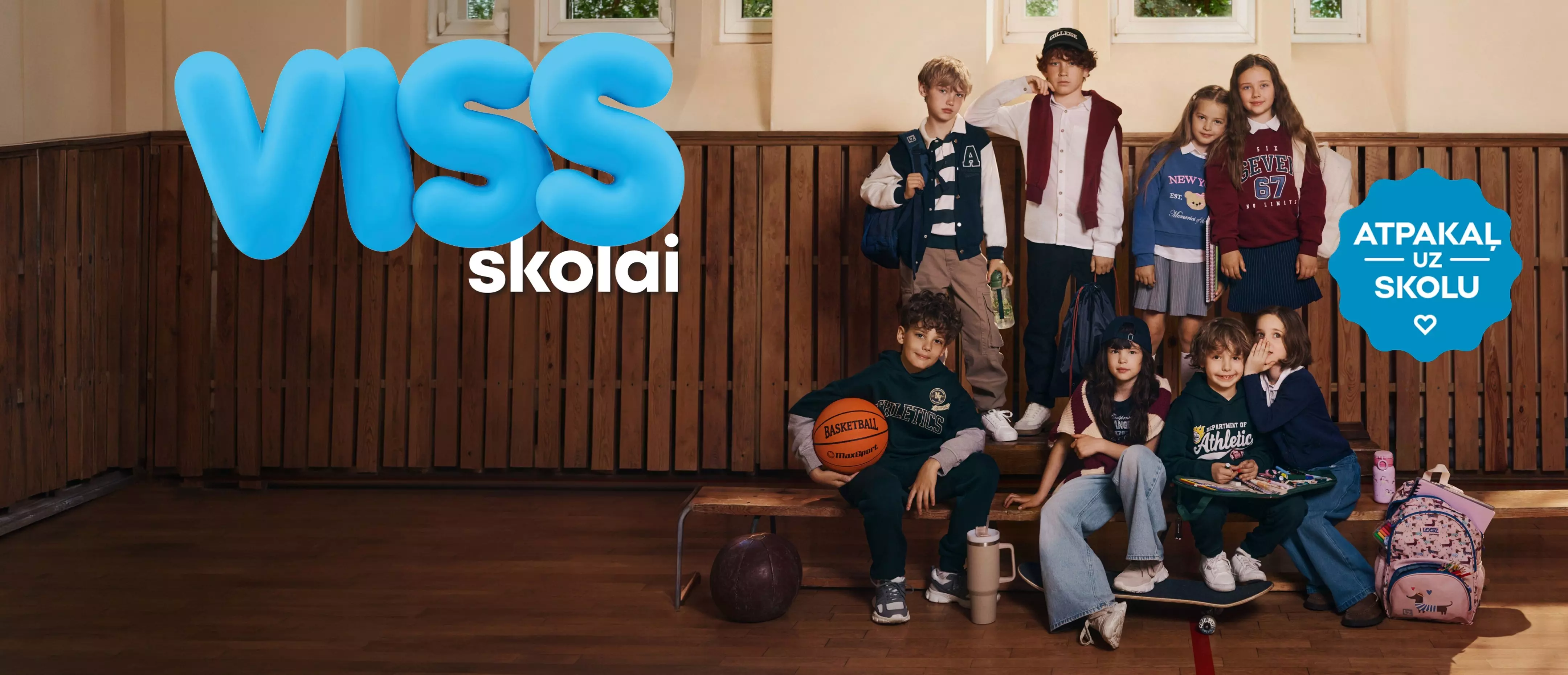 Pepco bērni skolas apģērbos ar somām un sporta inventāru skolas foajē ar tekstu VISS skolai.