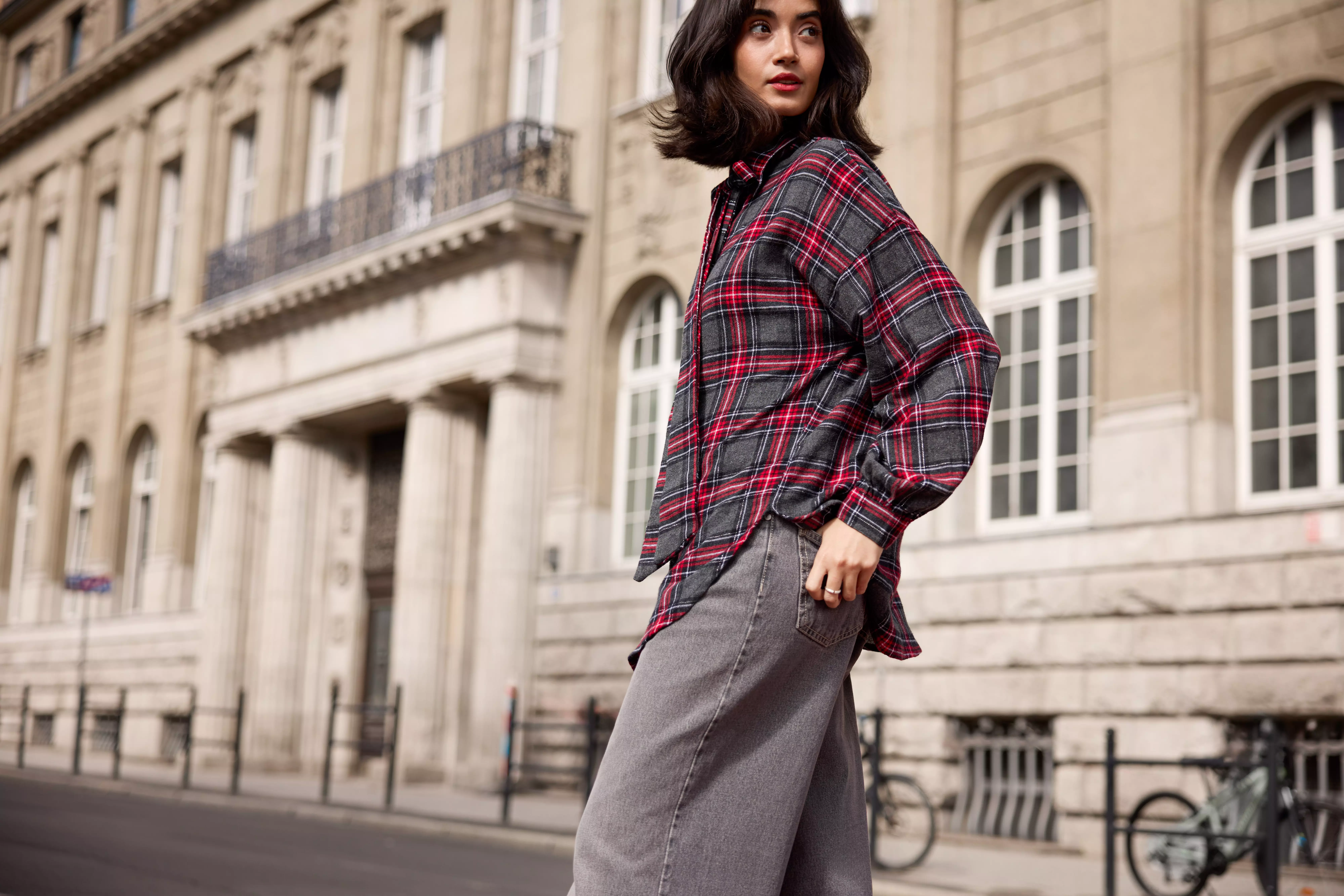 Pepco model wearing a red and grey checked shirt and grey jeans, walking on a city street.