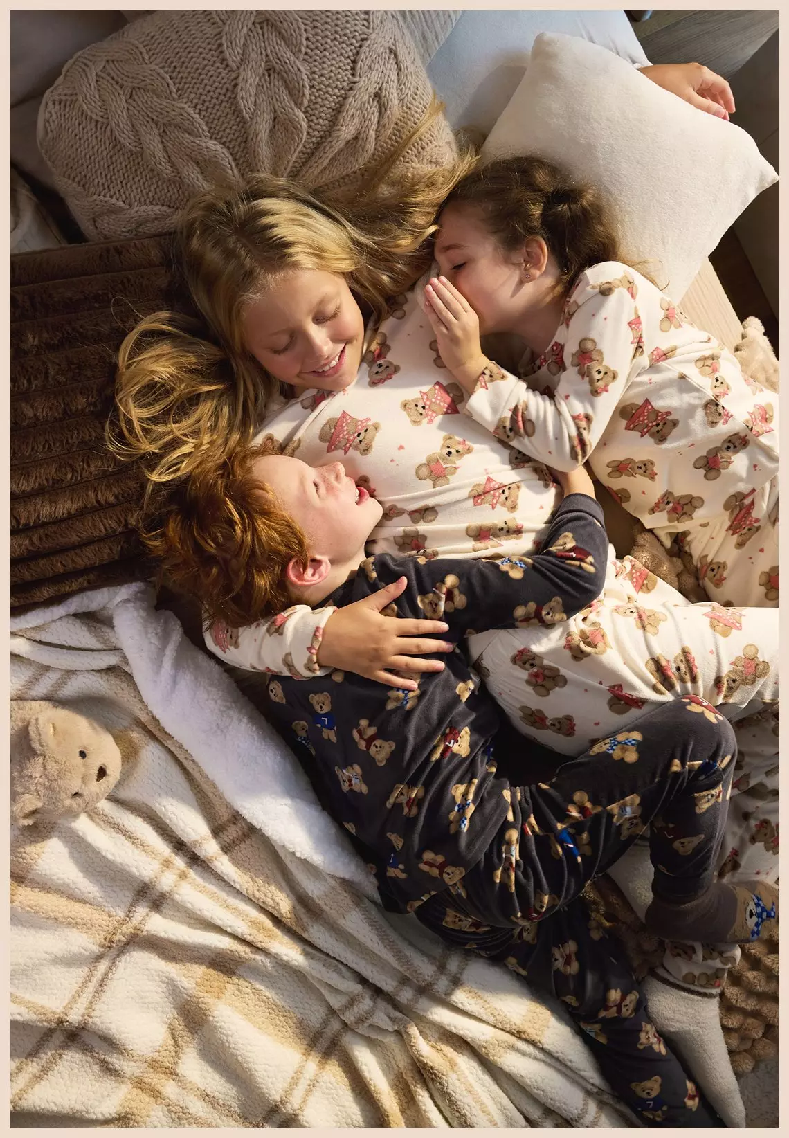 Tres niños riendo juntos en la cama vistiendo pijamas con estampado de ositos de Pepco.