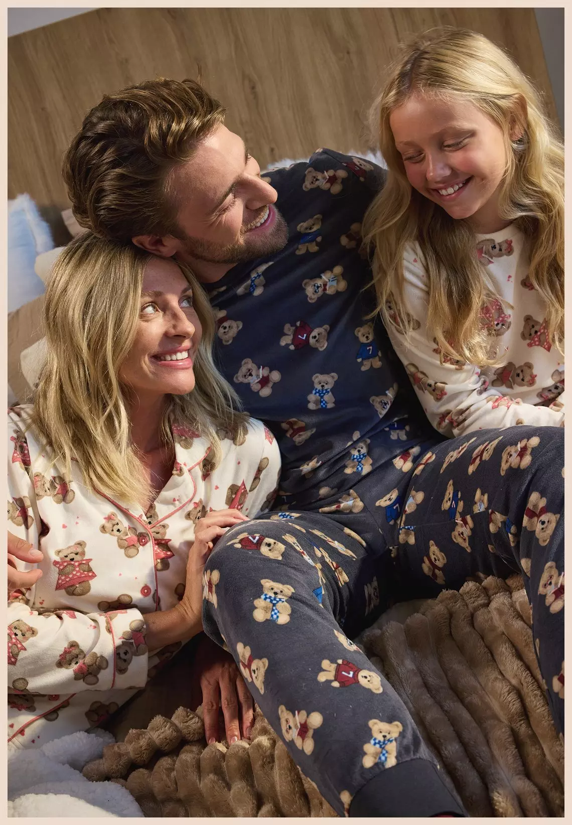 Familia feliz vistiendo pijamas a juego de Pepco con estampado de ositos, relajándose juntos en la cama.