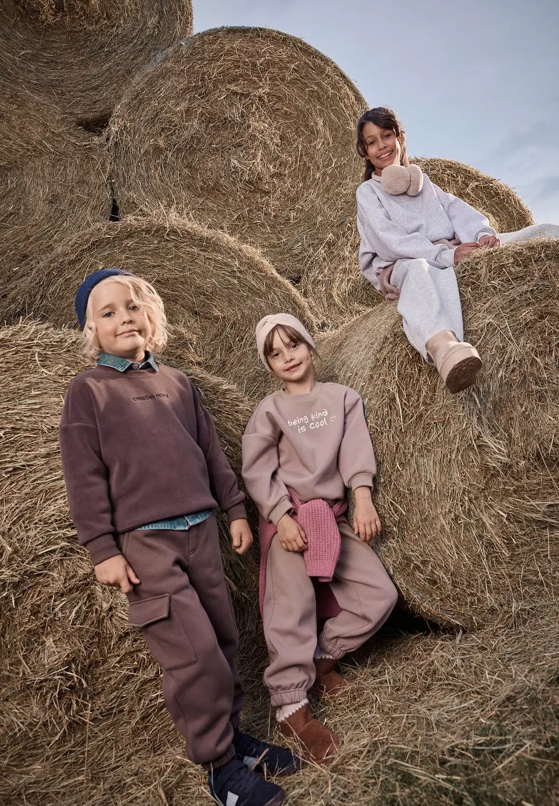 Tres niñas sonrientes vistiendo chándales Pepco posando sobre balas de heno en el campo.