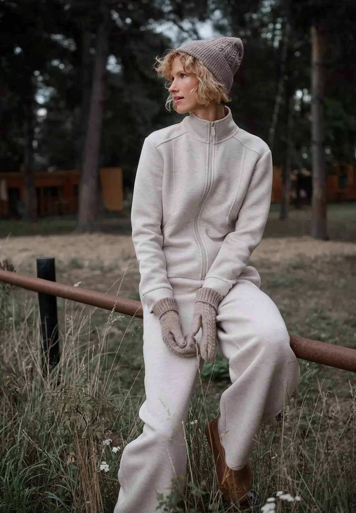 Mujer sentada al aire libre con chándal beige, gorro y guantes de punto de Pepco.