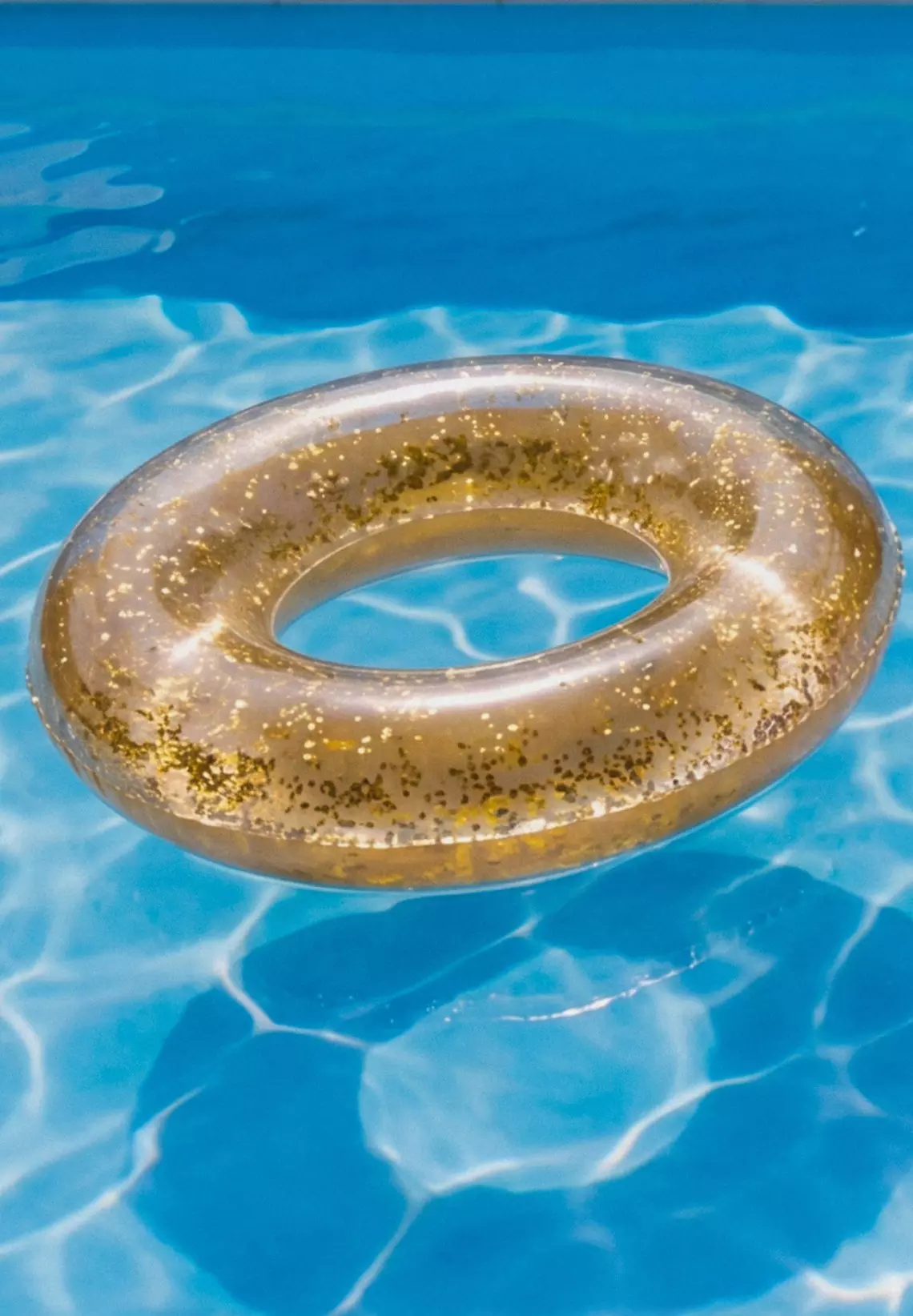 Clear inflatable swim ring with gold glitter floating on blue swimming pool water.